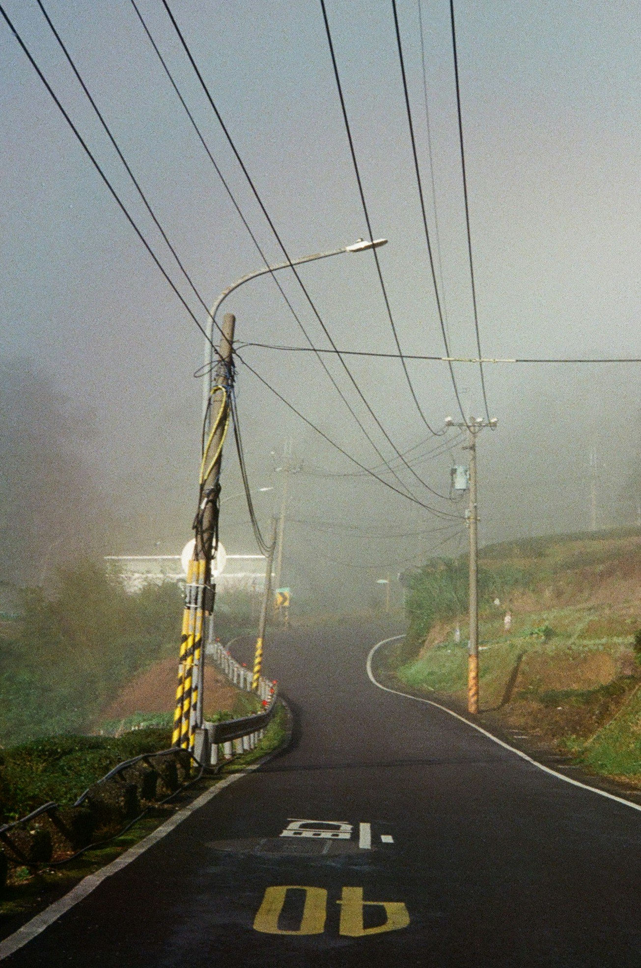 霧のかかった田舎道を走る電柱と道路標示のある風景