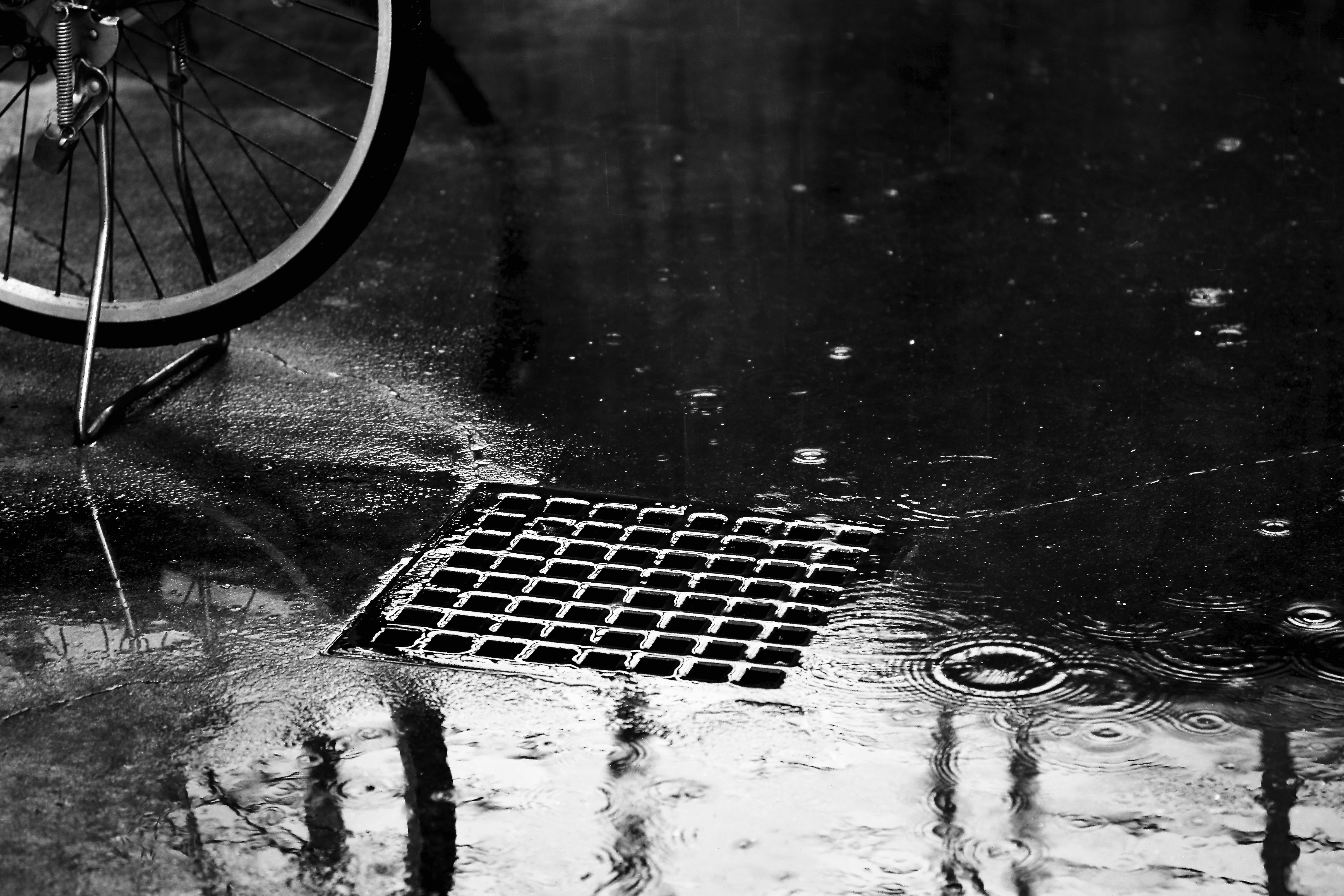 雨の路面に自転車の車輪と排水グレーチングがある路地