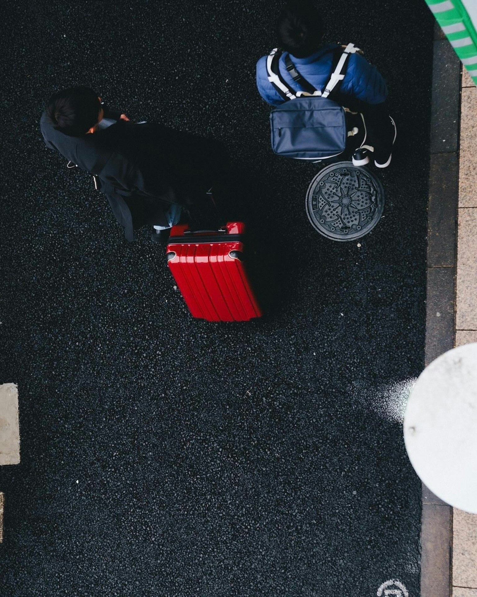 Cảnh đường phố nhìn từ trên cao với một người mang vali đỏ và một người khác mang túi xanh lam