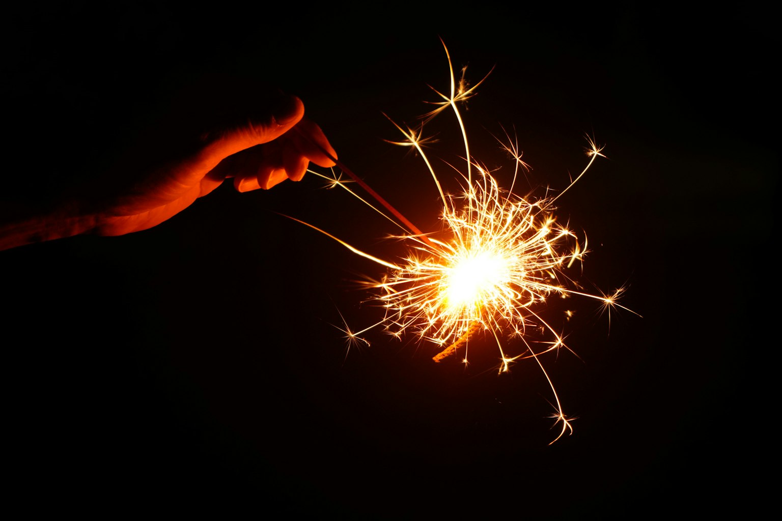 A hand holding a sparkling firework in the dark