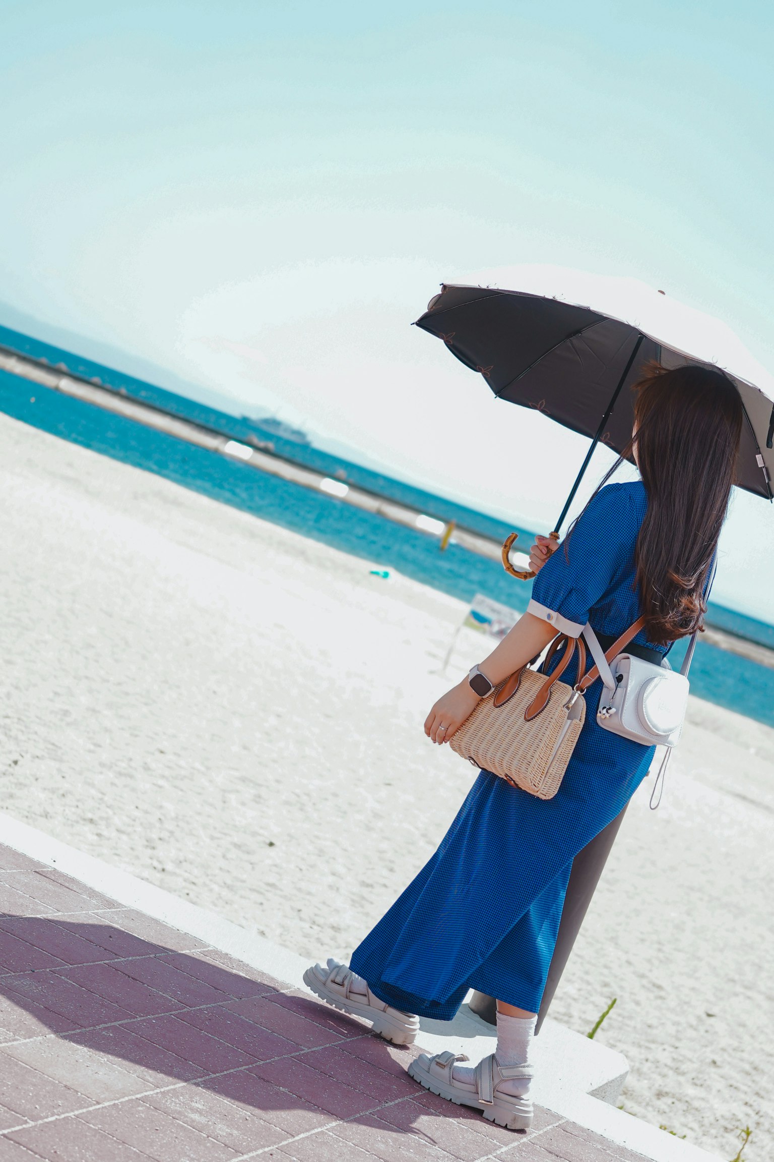 Una donna in abito blu che tiene un ombrello mentre cammina lungo la spiaggia