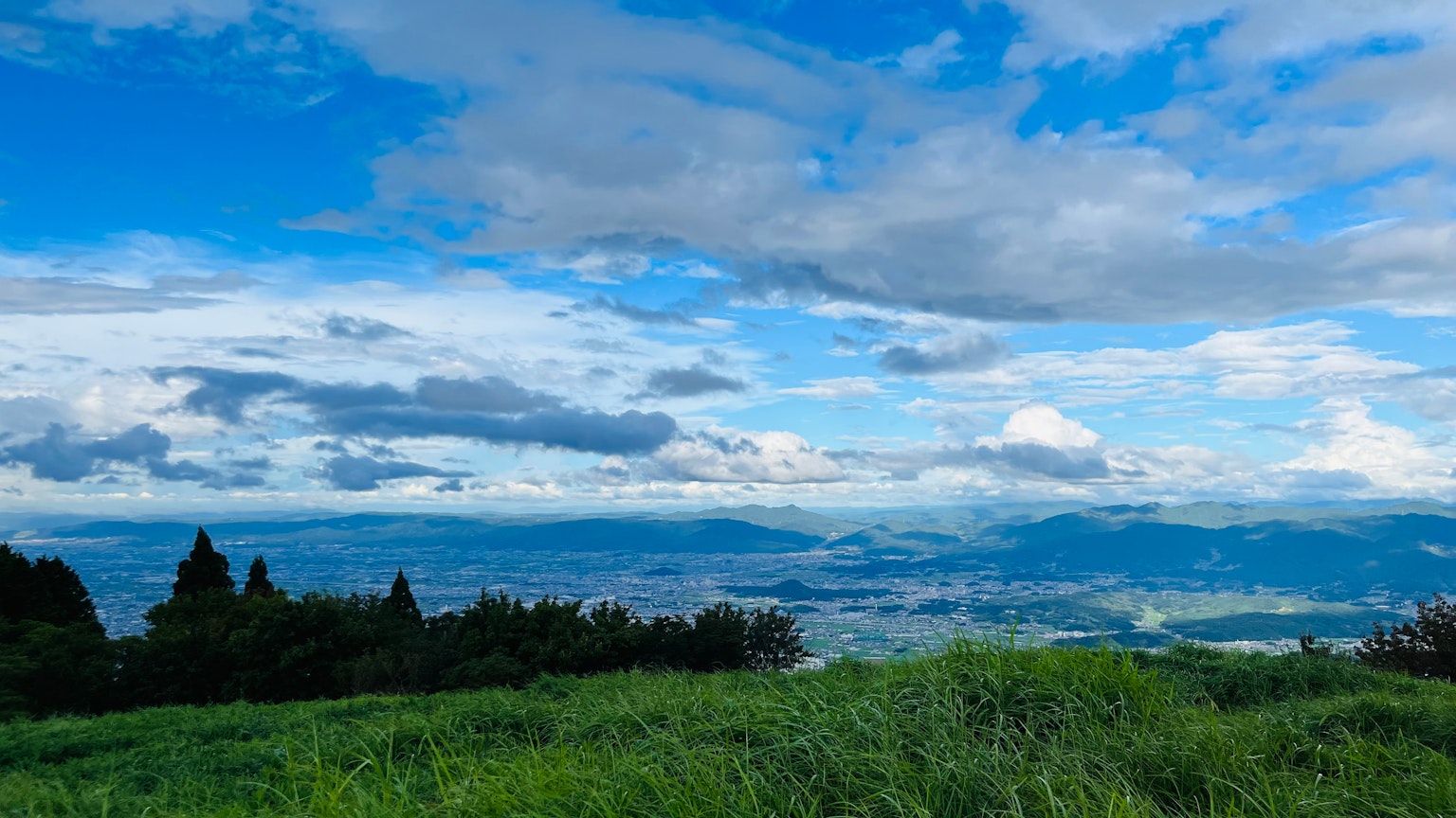 蓝天和云彩的风景 绿色草地延展 远处可见山脉和城市