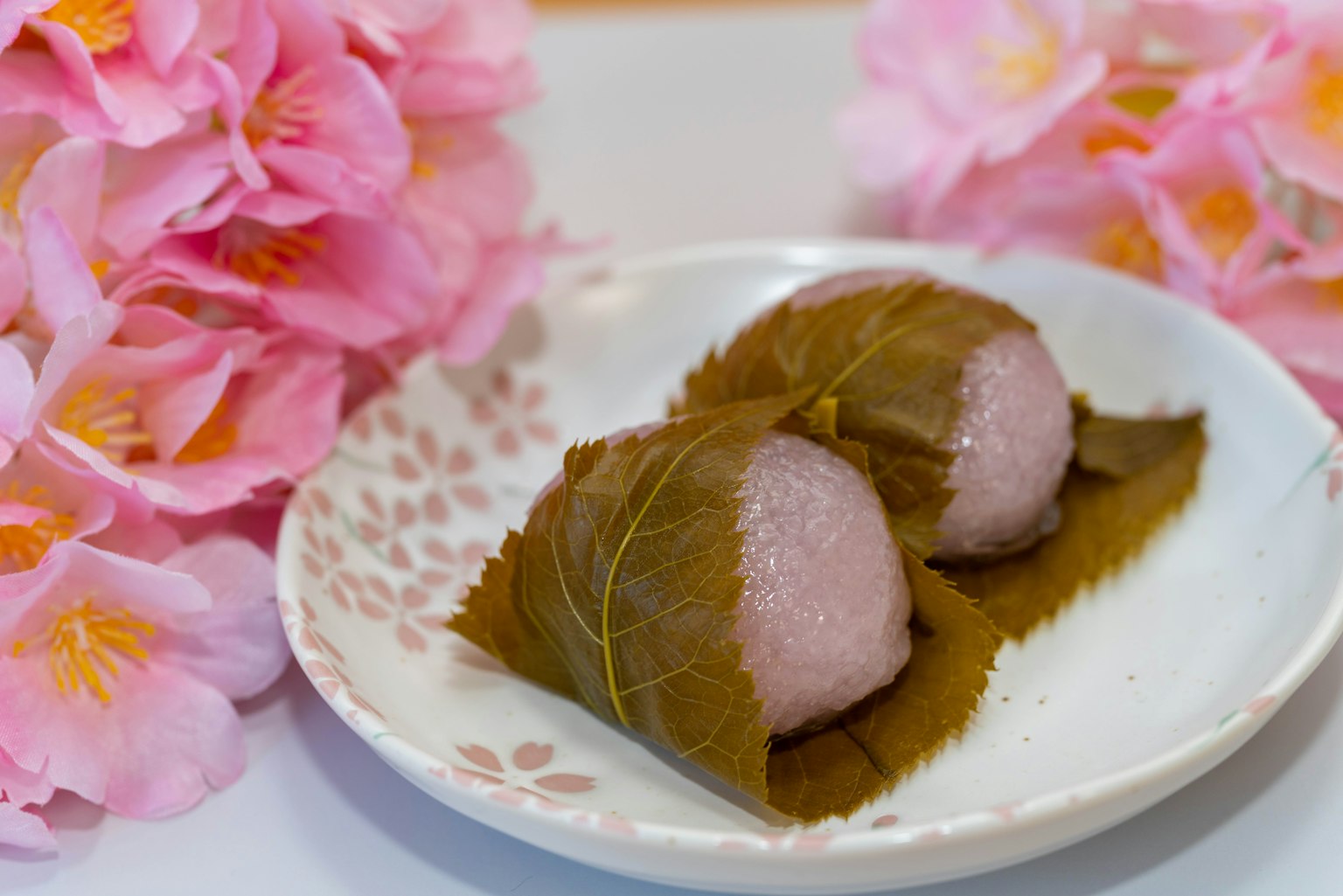 체리 블라썸 잎에 싸인 일본 모찌와 분홍색 꽃이 배경에 있는 모습