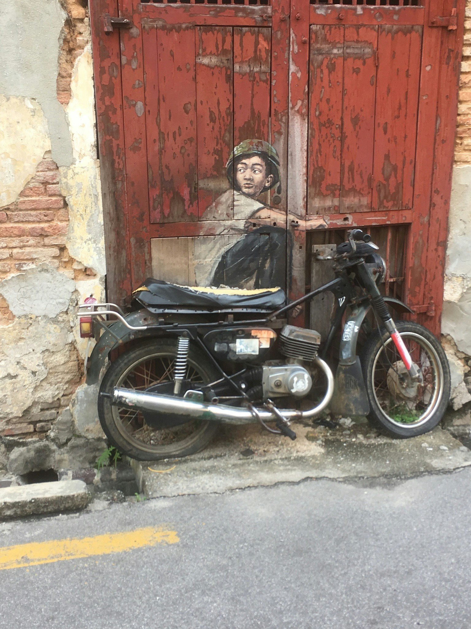 Ein Motorrad, das vor einer alten roten Tür mit einem Wandgemälde eines Kindes parkt