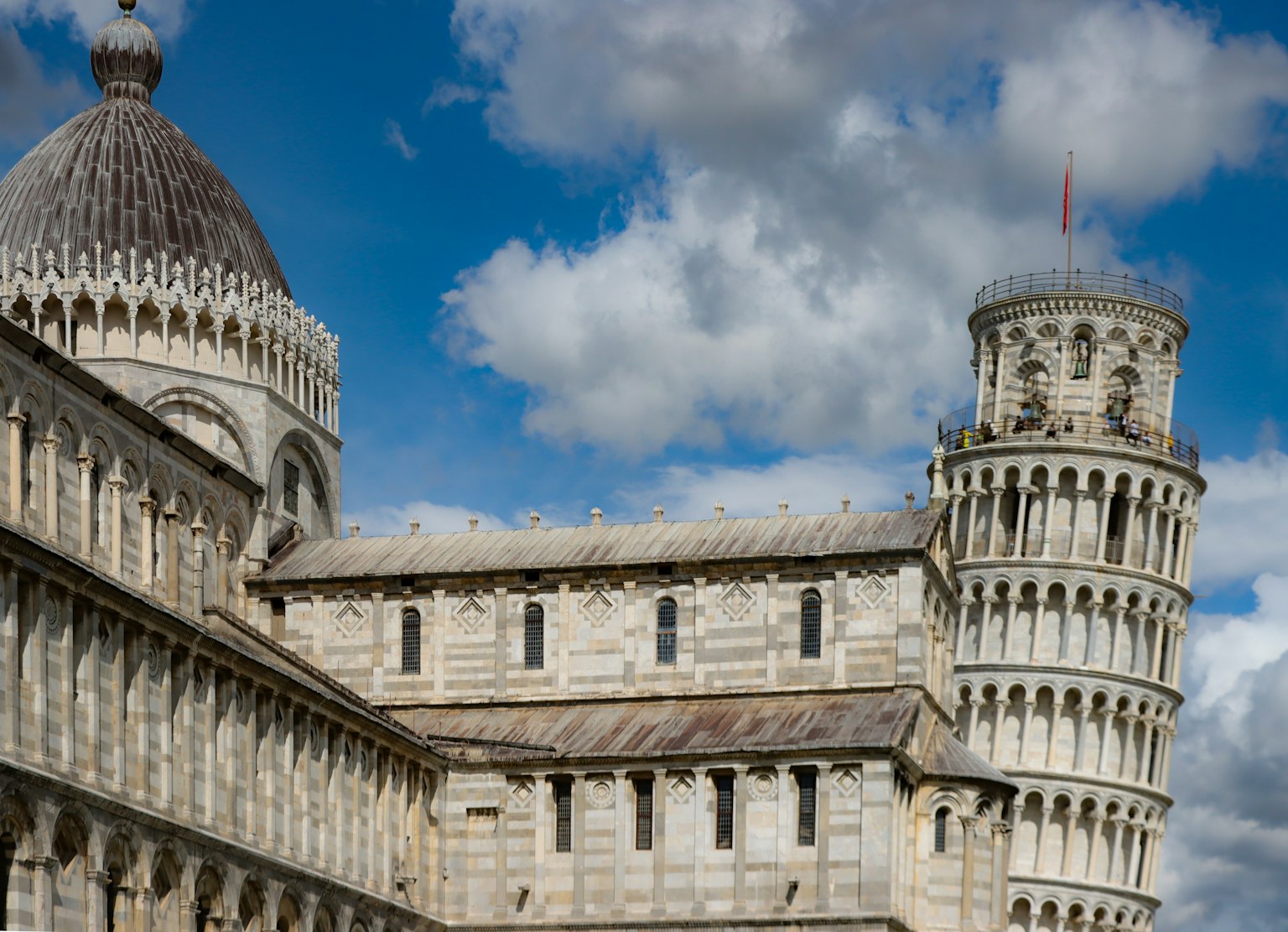 Image of the Leaning Tower of Pisa and surrounding architecture with white clouds and blue sky