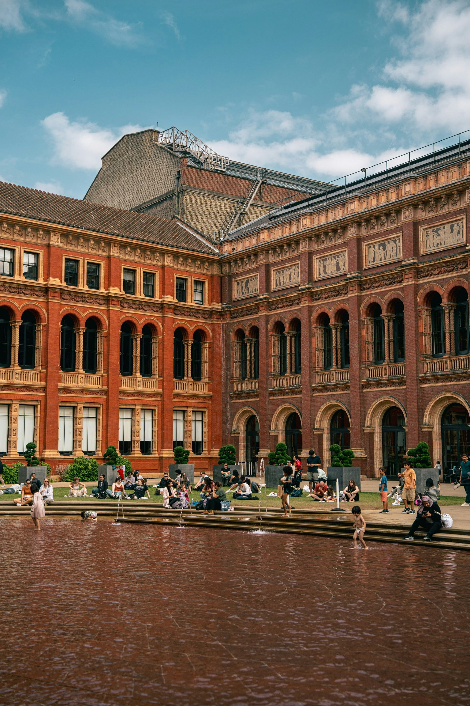 Blick auf den Innenhof des Victoria and Albert Museums mit roten Backsteingebäuden und einem Teich