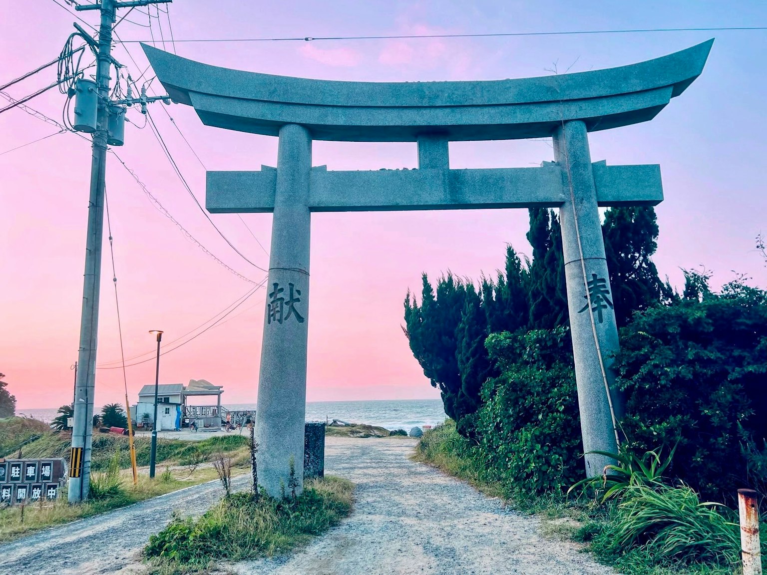 Cổng torii lớn đứng trên con đường dẫn ra biển với bầu trời hoàng hôn