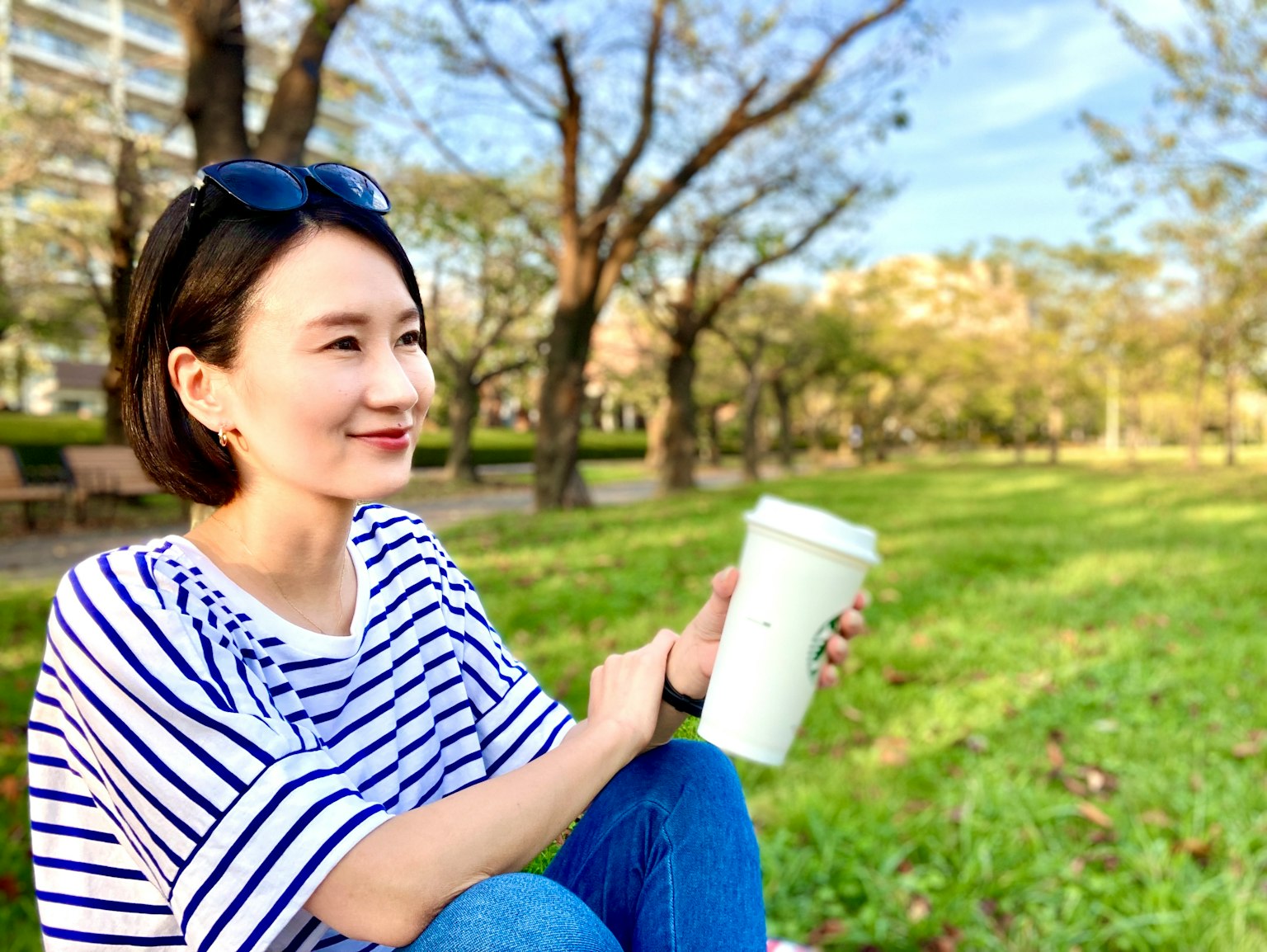 스트라이프 셔츠를 입고 흰 컵을 들고 있는 여성, 공원에서 자연을 즐기고 있음