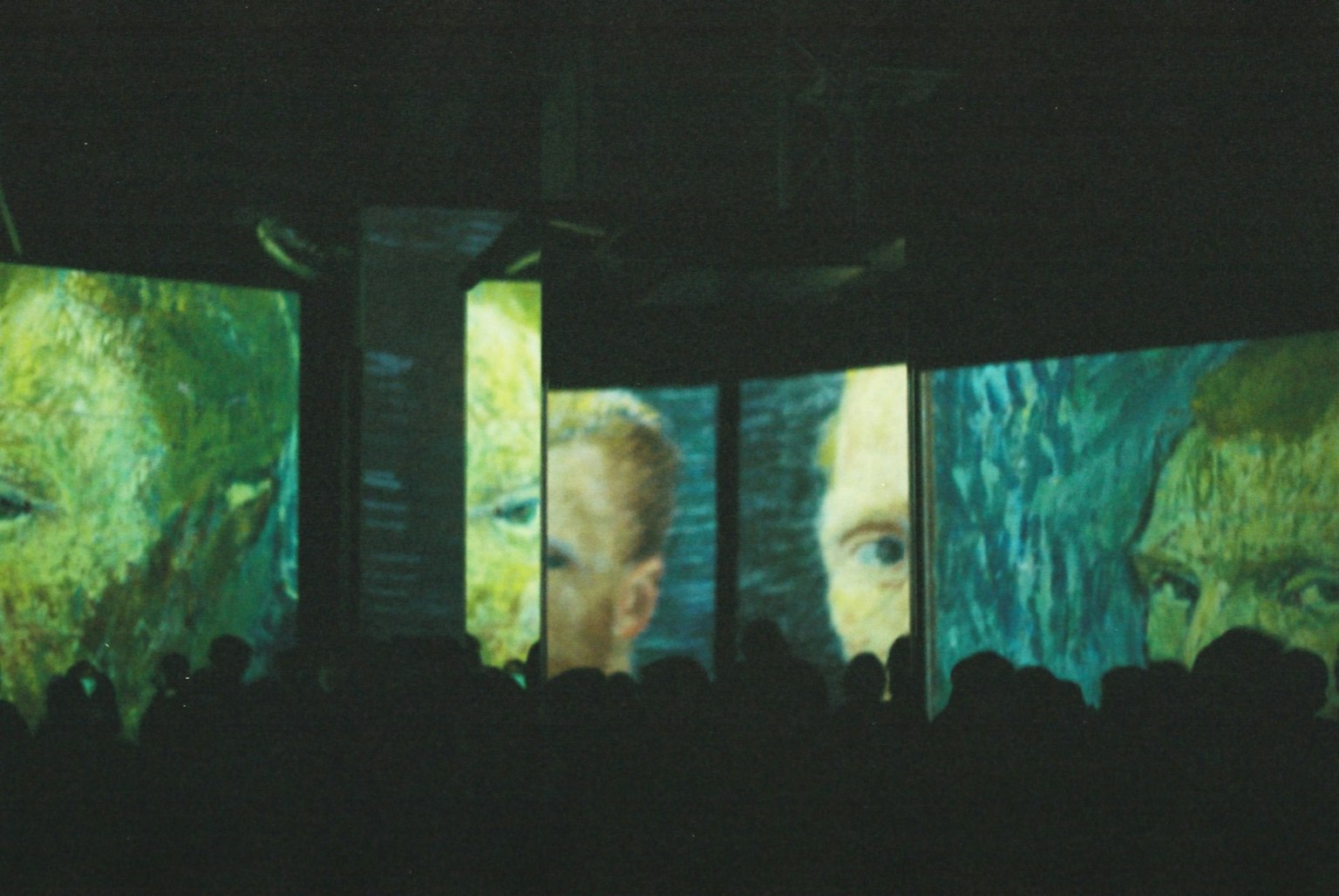 A dark room filled with people viewing projections of Vincent van Gogh's artwork