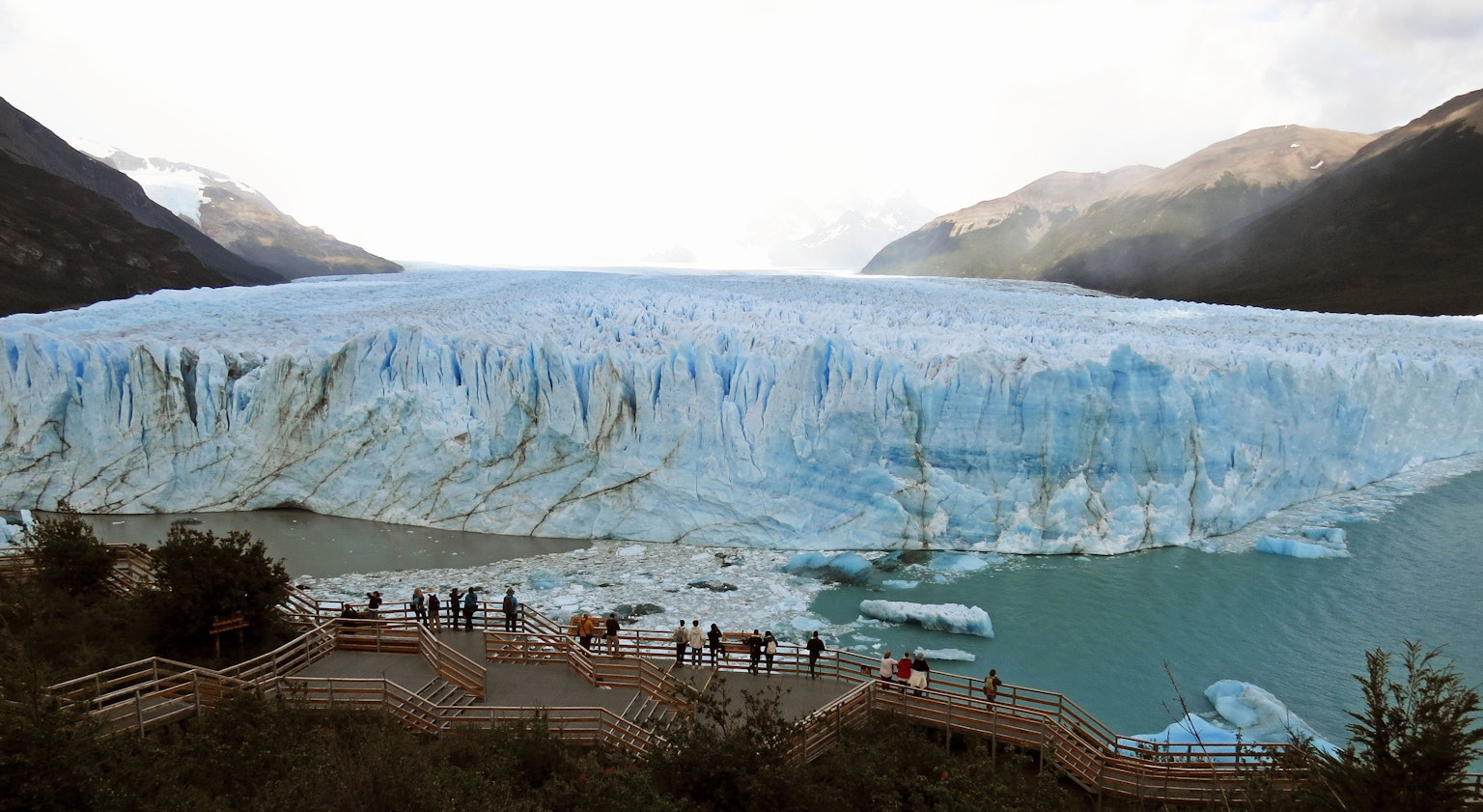 Eine blaue Gletscherwand mit Touristen im Vordergrund