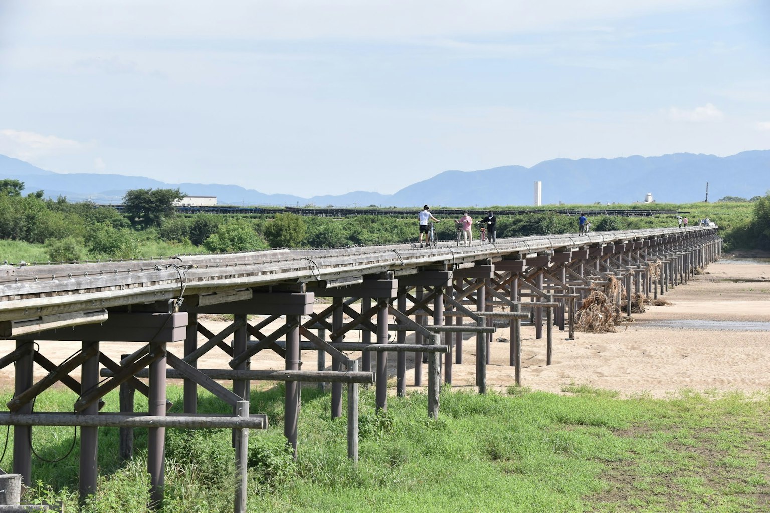 Pont en bois s'étendant sur un paysage verdoyant avec des montagnes en arrière-plan