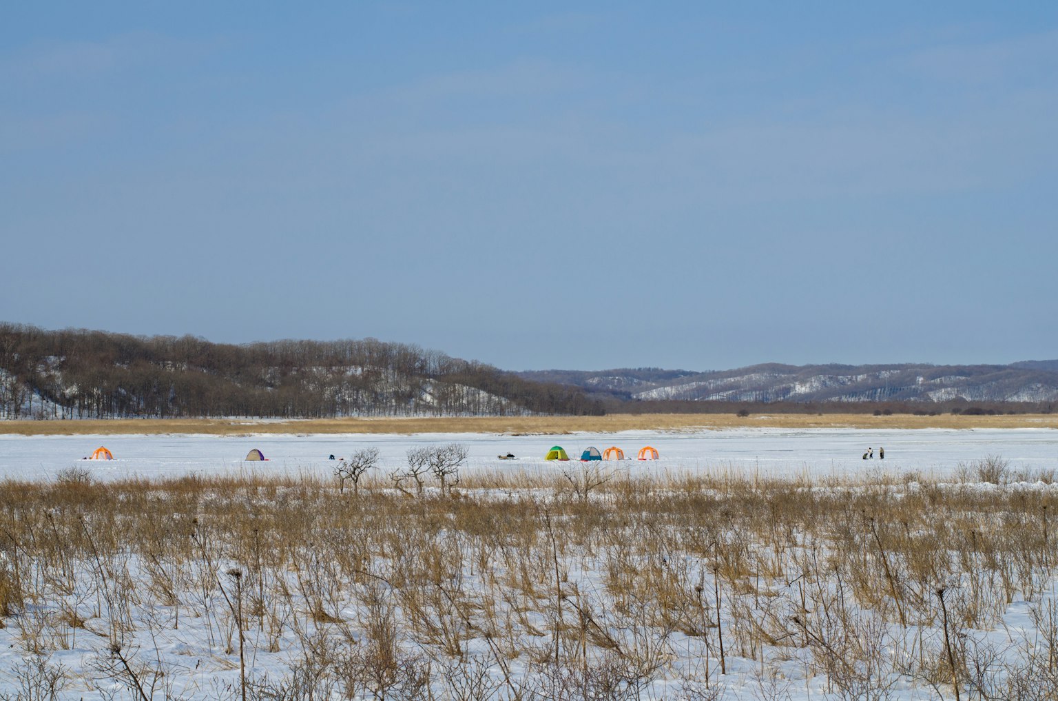 Groupe de tentes de camping sur un lac recouvert de neige sous un ciel bleu