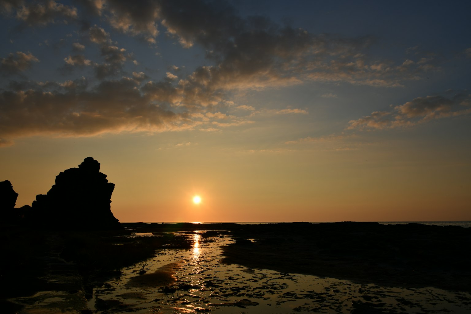 Scène de coucher de soleil côtier avec des rochers et des reflets sur l'eau