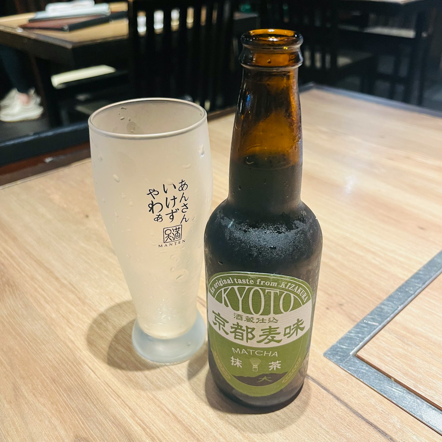 一瓶京都啤酒和一个透明玻璃杯放在木桌上