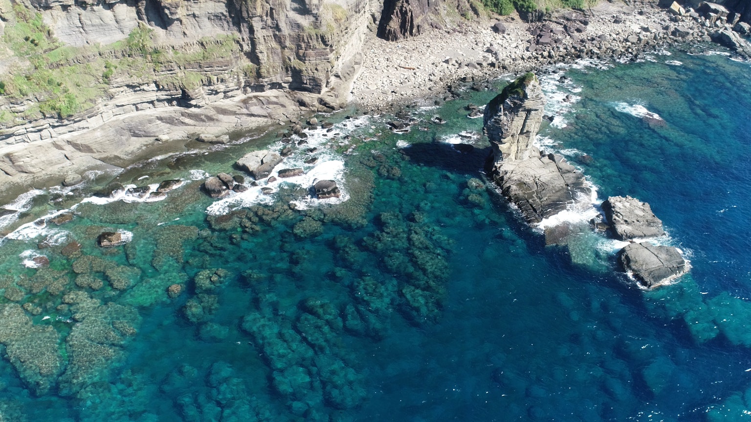 Luftaufnahme einer felsigen Küste mit klarem blauen Wasser und sichtbaren Unterwasserfelsen