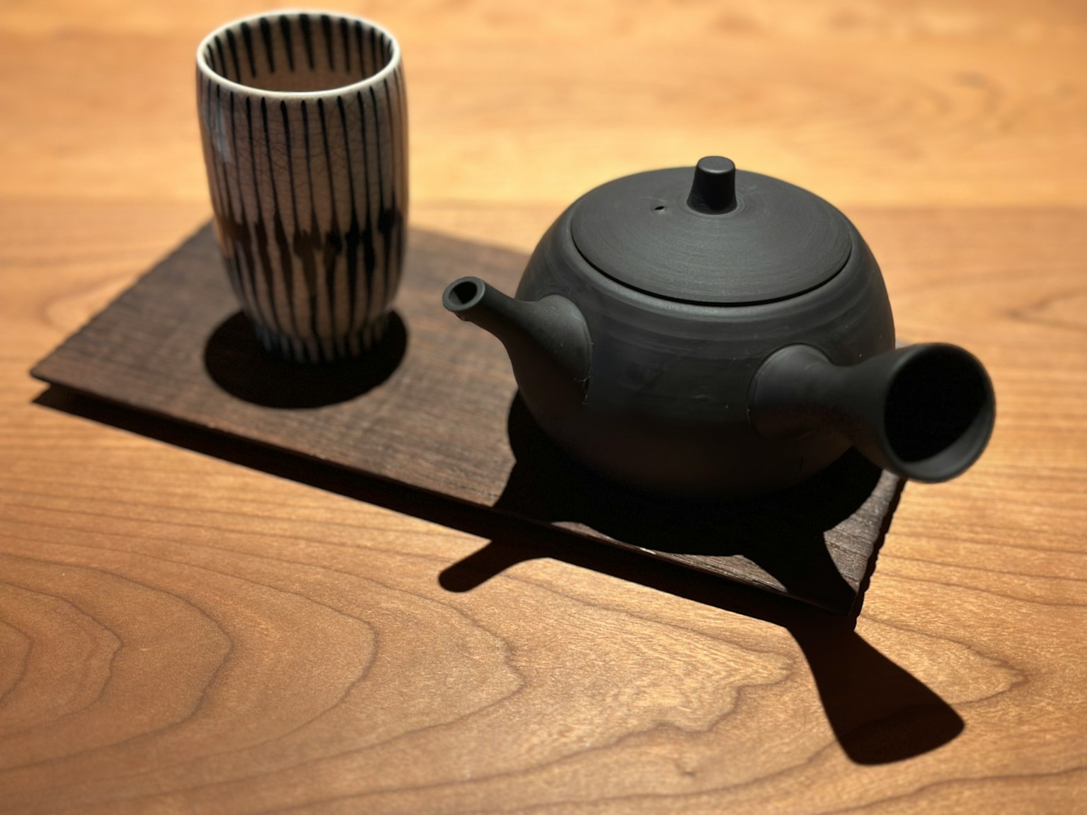 A black teapot and striped teacup placed on a wooden tray