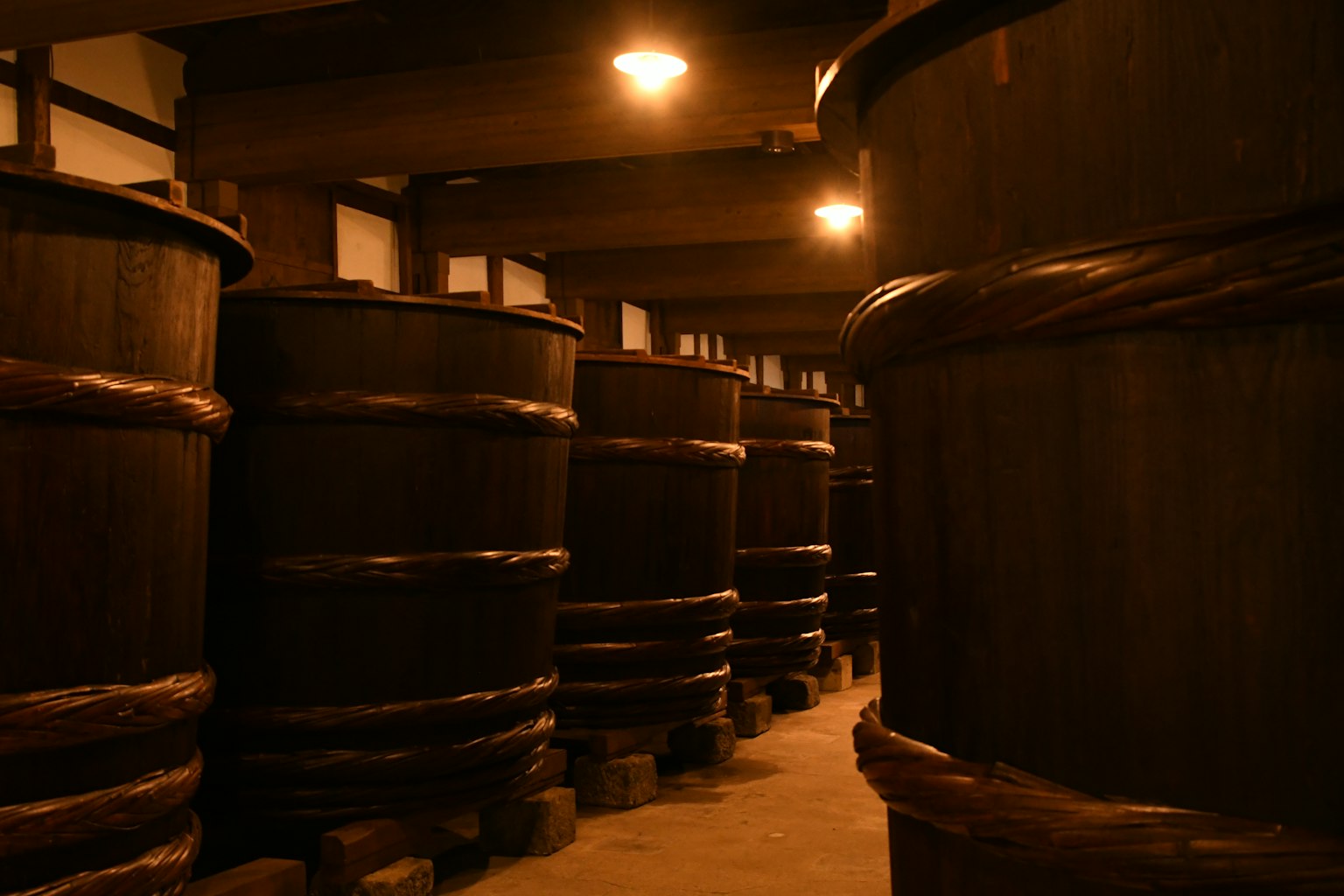 Intérieur d'une brasserie de saké avec de grands fûts en bois dans un espace faiblement éclairé