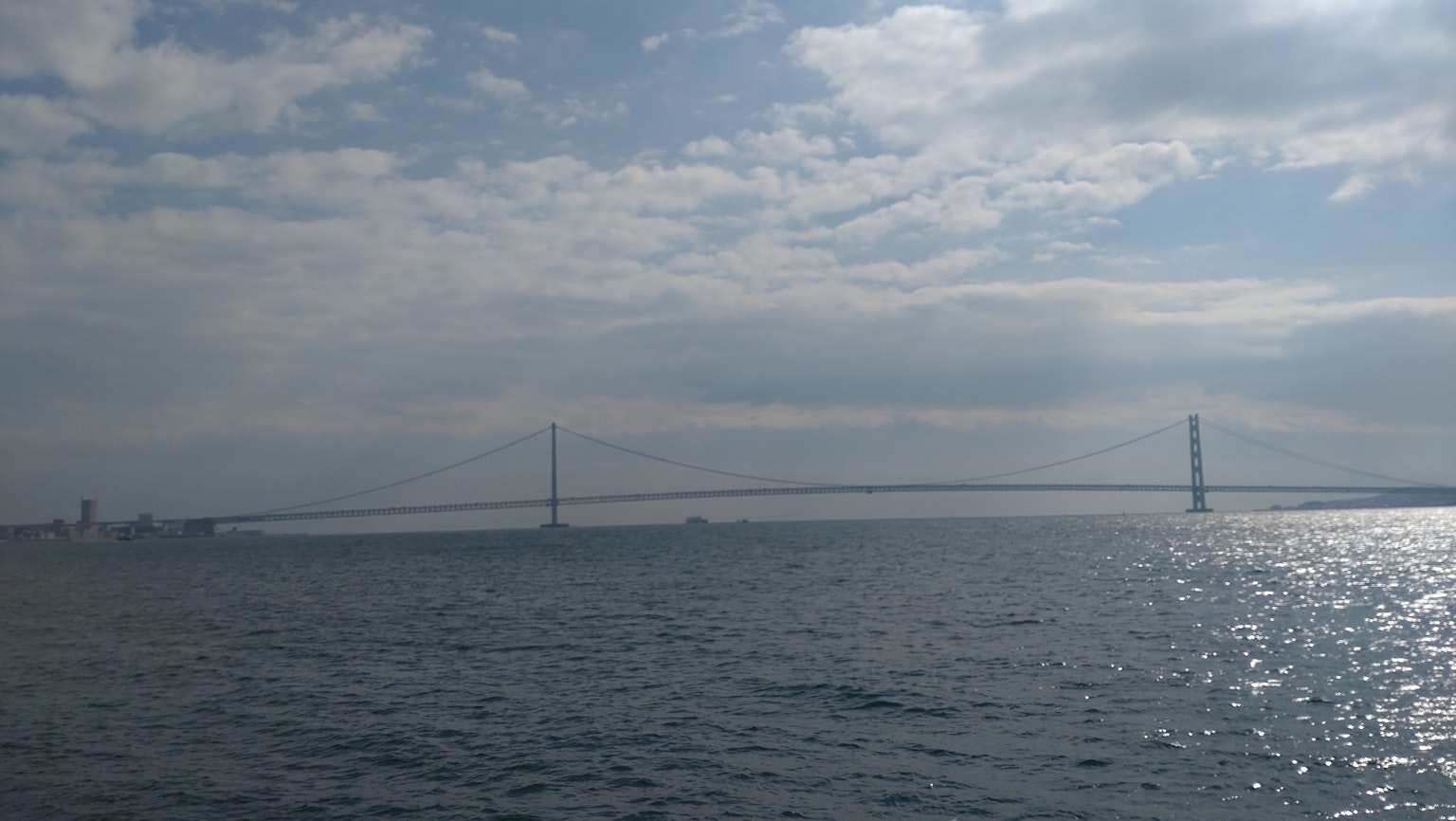 View of a bridge spanning a blue sea under a cloudy sky