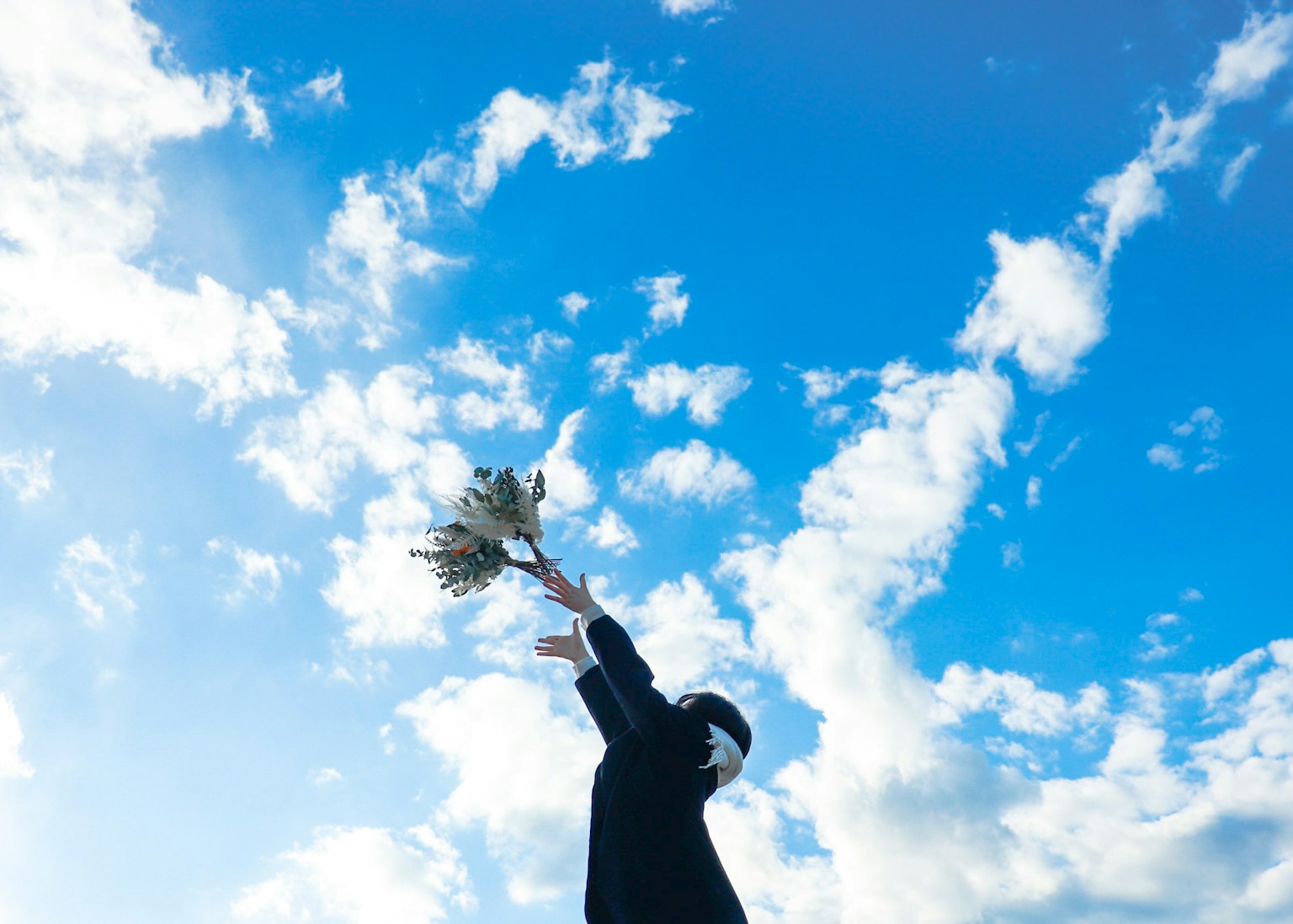 青空の下で花束を持ち上げる人物のシルエット