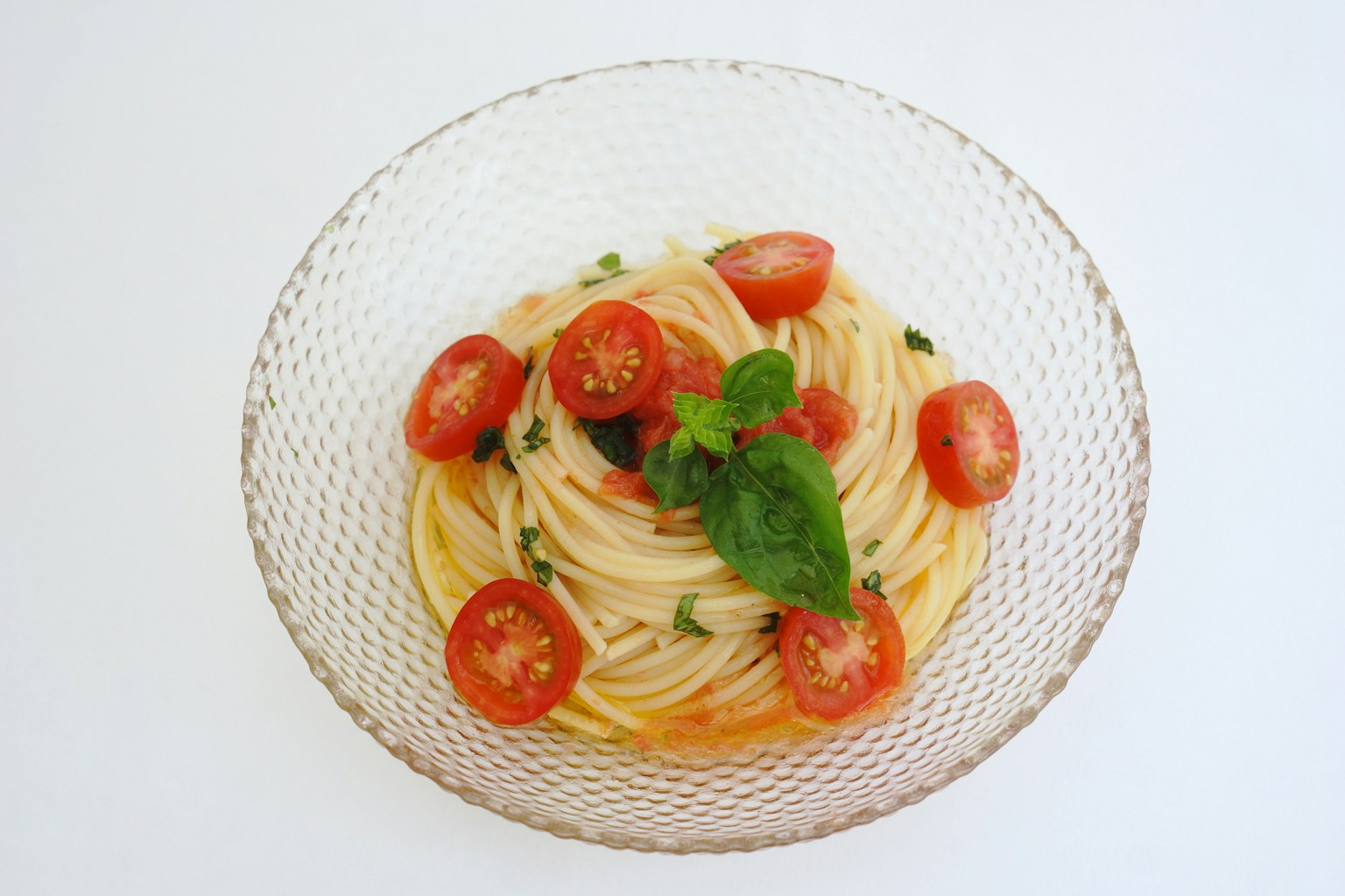 Spaghetti mit Kirschtomaten und Basilikum in einer klaren Glasschüssel serviert