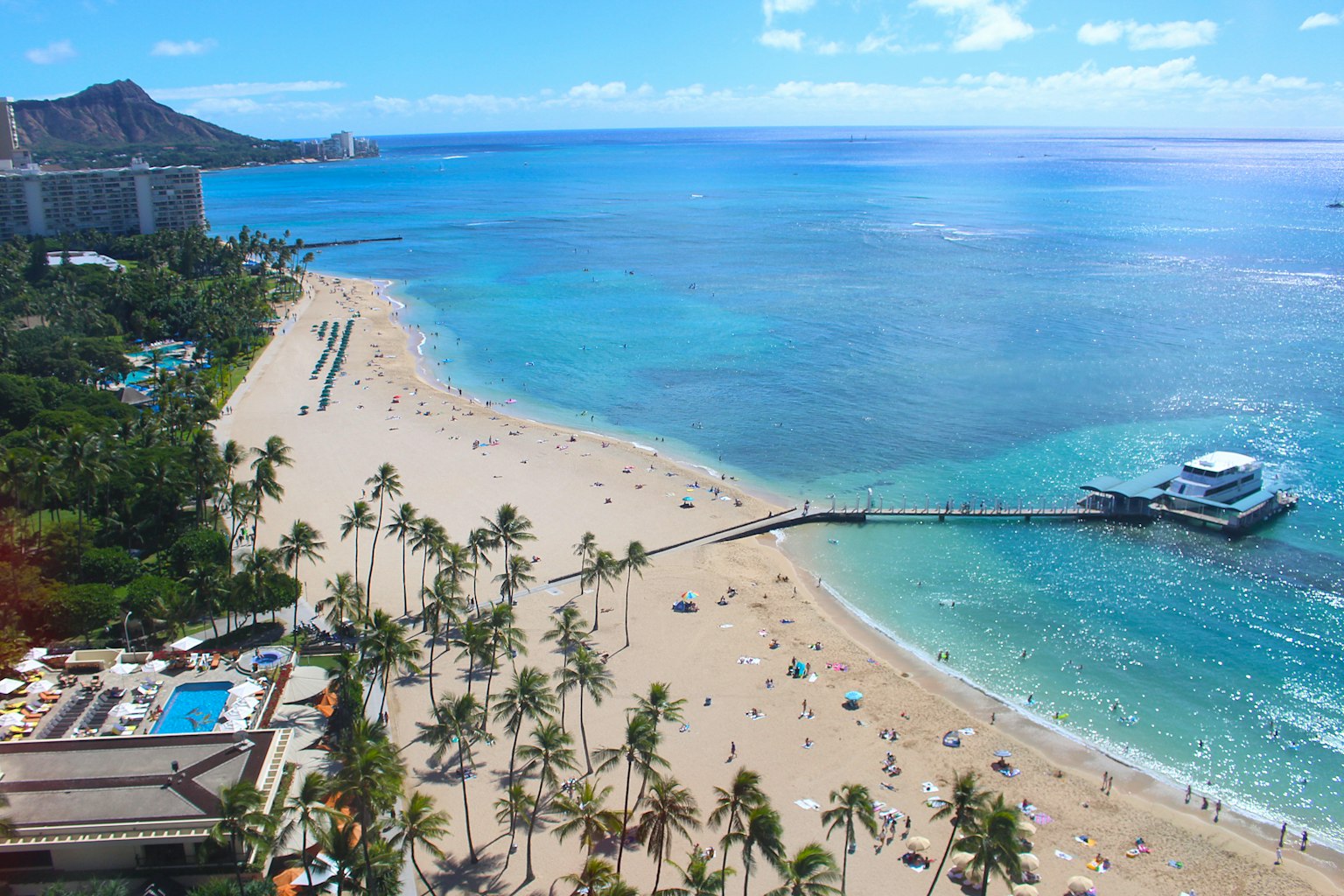 A scenic beach view with blue ocean and white sand Many people enjoying the beach near palm trees and a pier