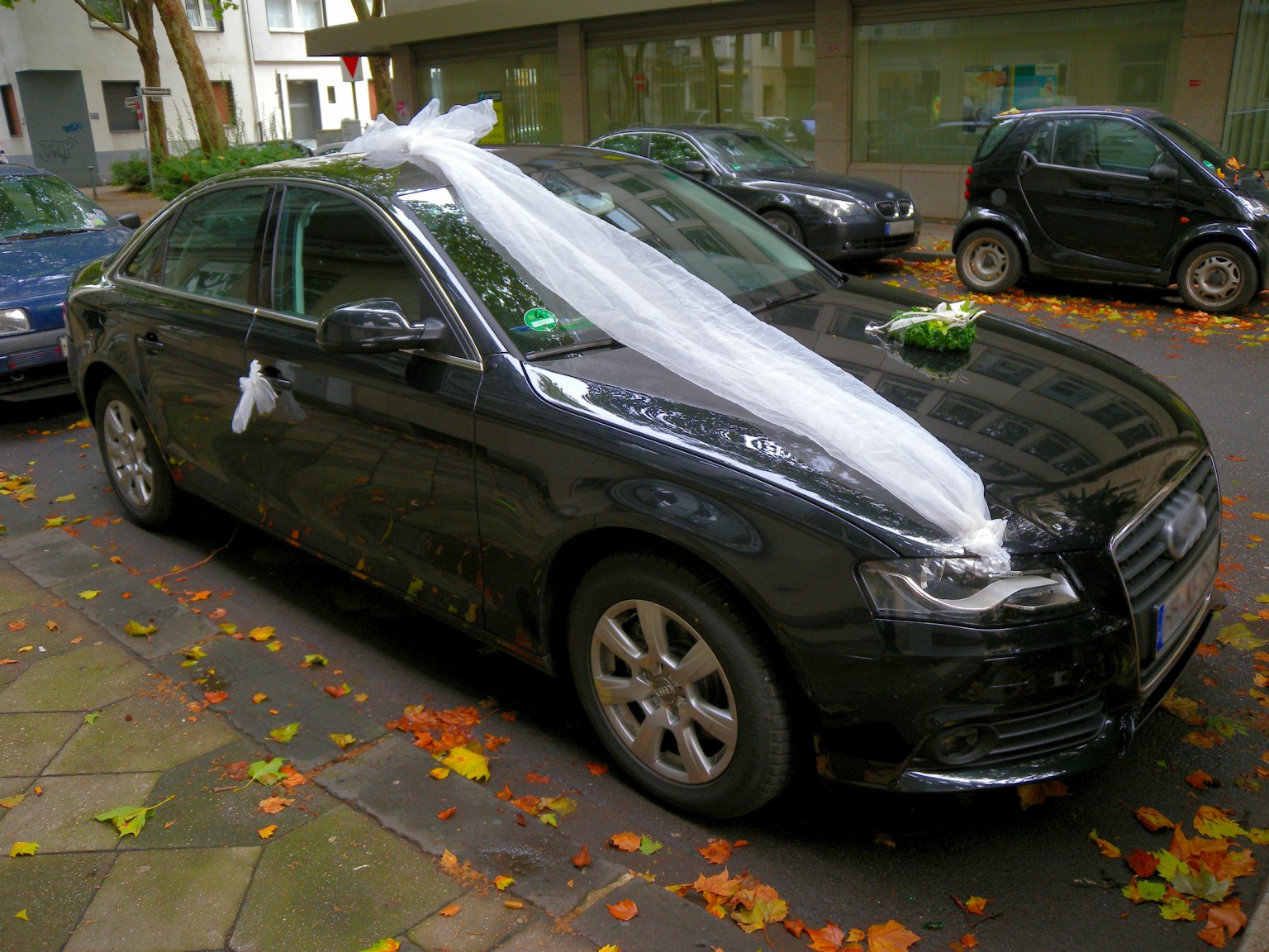 Voiture noire décorée avec des rubans blancs et des fleurs pour un mariage