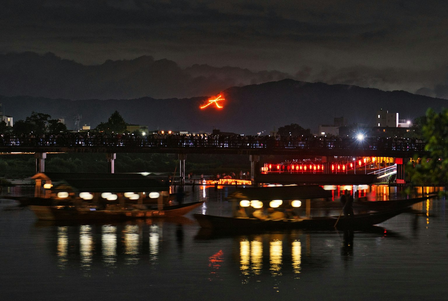 Bateaux sur une rivière la nuit avec un caractère de feu brillant sur la montagne