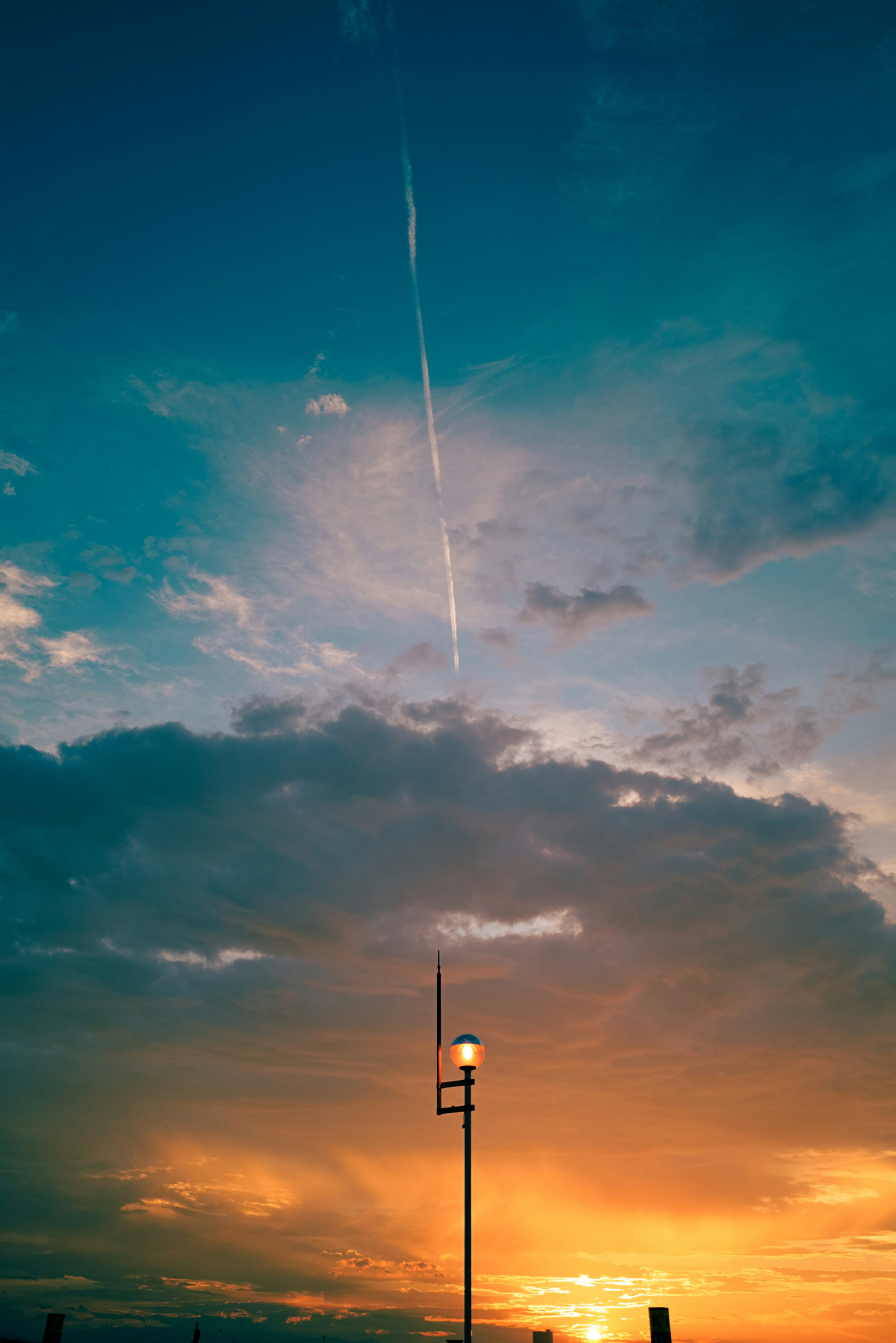 夕焼け空に伸びる光の筋と街灯のシルエット