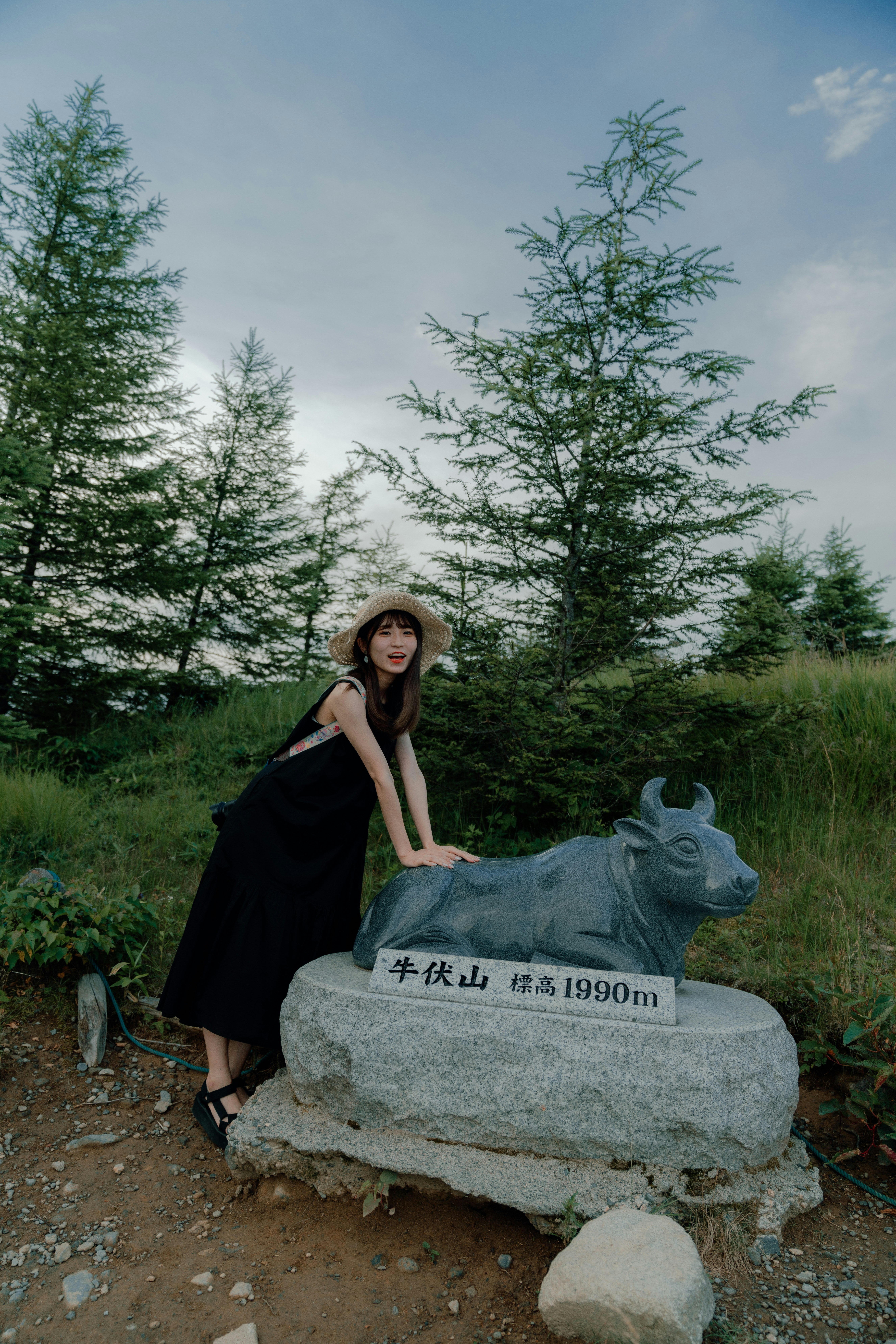草地山路上，針葉林中站在石碑旁的女性