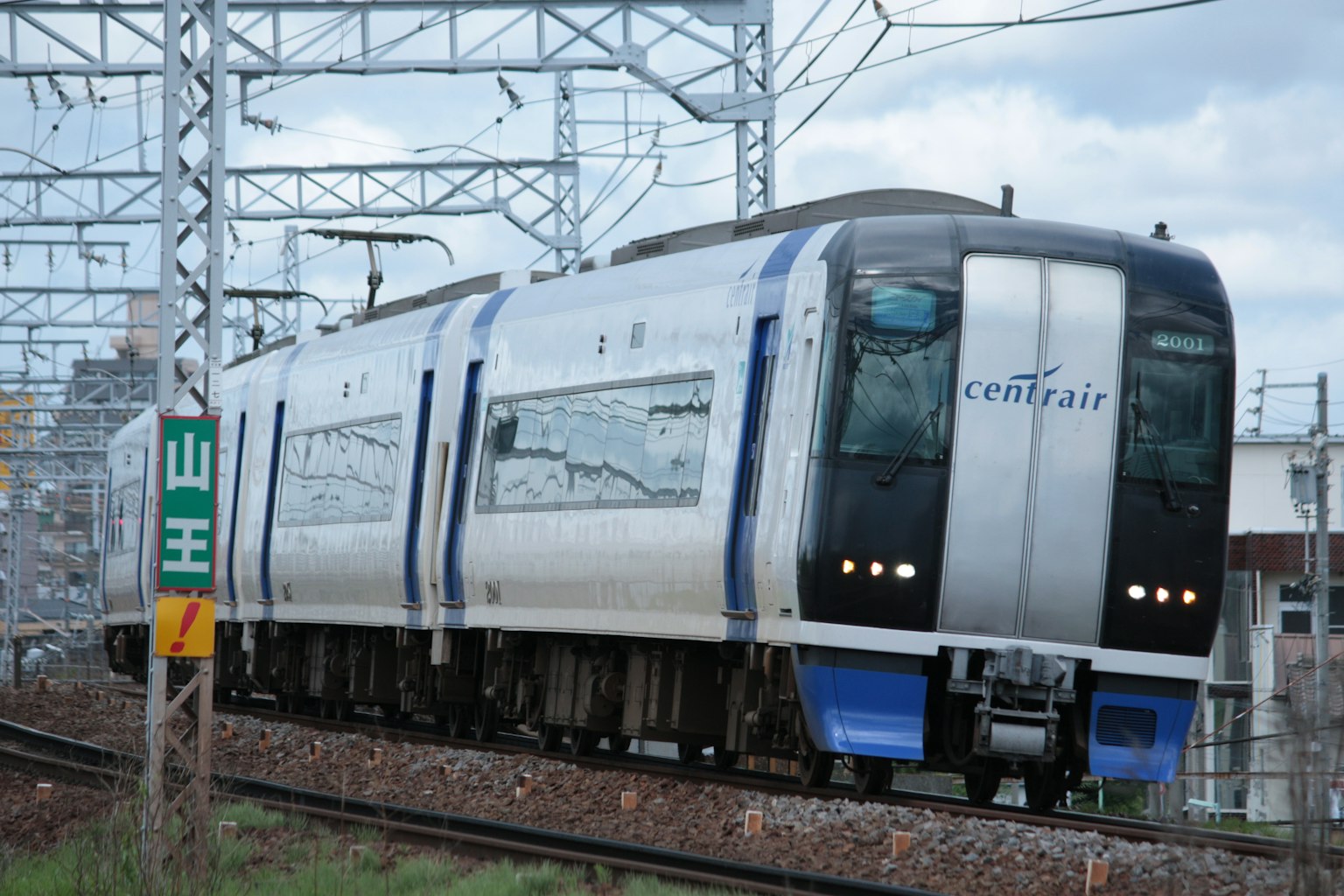 Un treno blu sta correndo sui binari con fili aerei e segnali visibili sullo sfondo