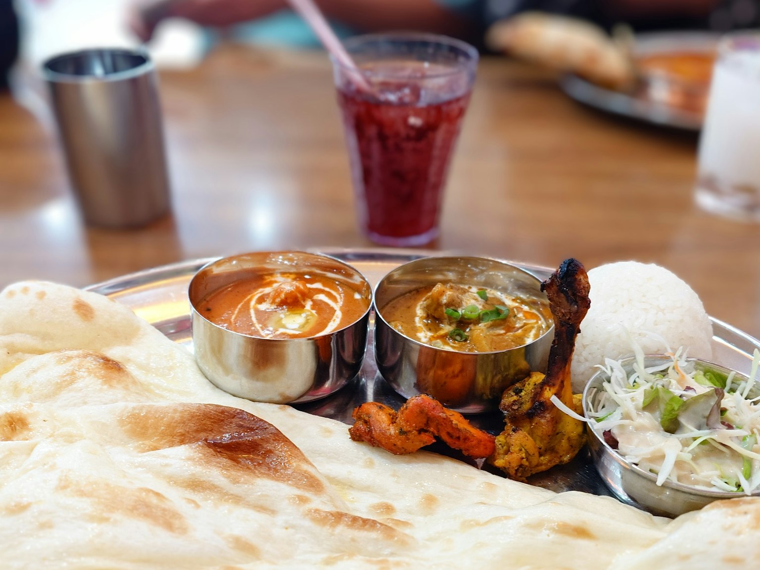 Piring masakan India dengan naan, kari, salad, dan minuman