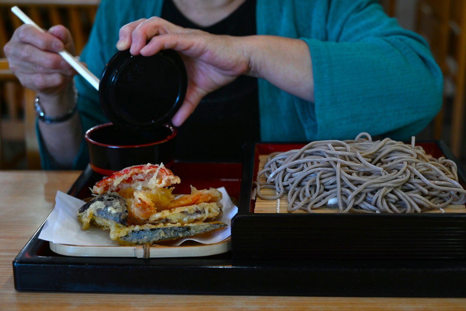 Sebuah tangan menuangkan saus di atas tempura dan mie soba