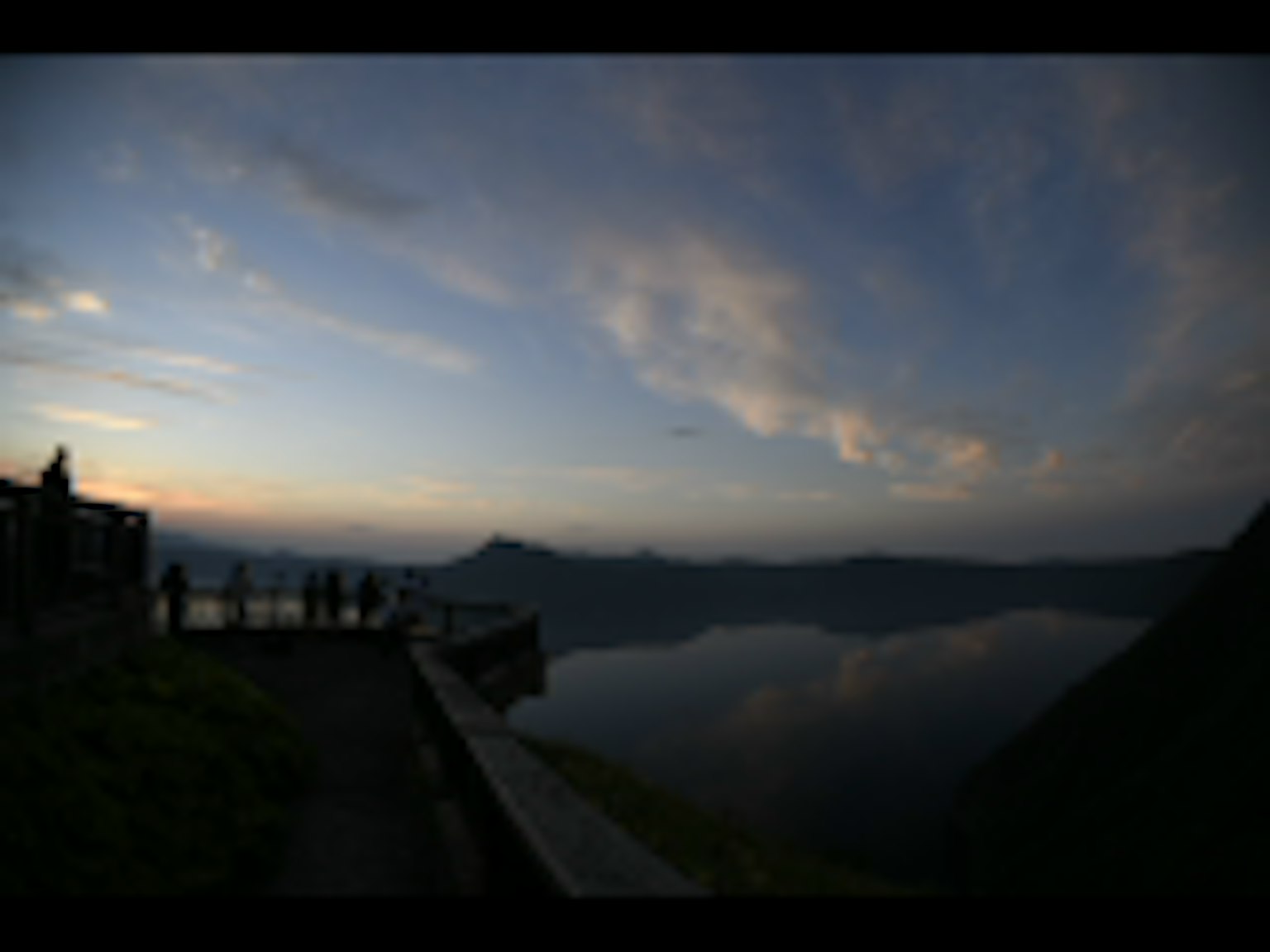 Vista escénica de un lago al atardecer con siluetas de montañas y un reflejo