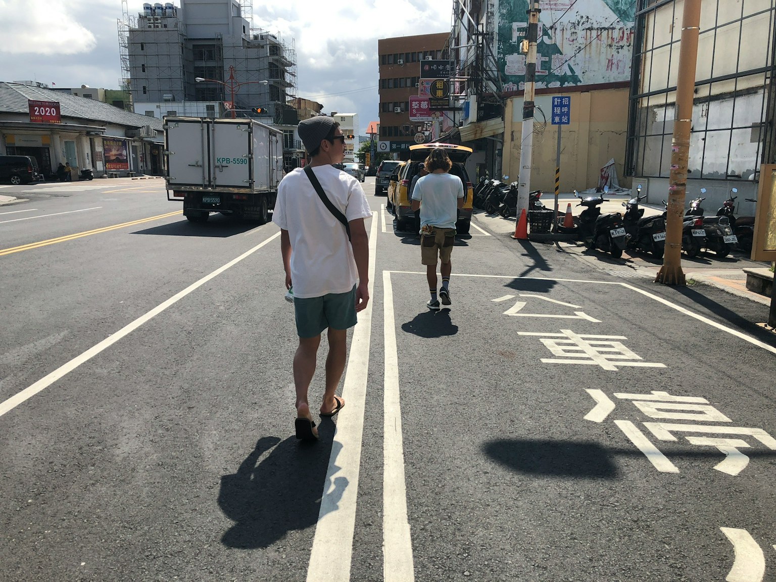 两名男子在城市街道上行走，背景中有公交车站标志和建筑物