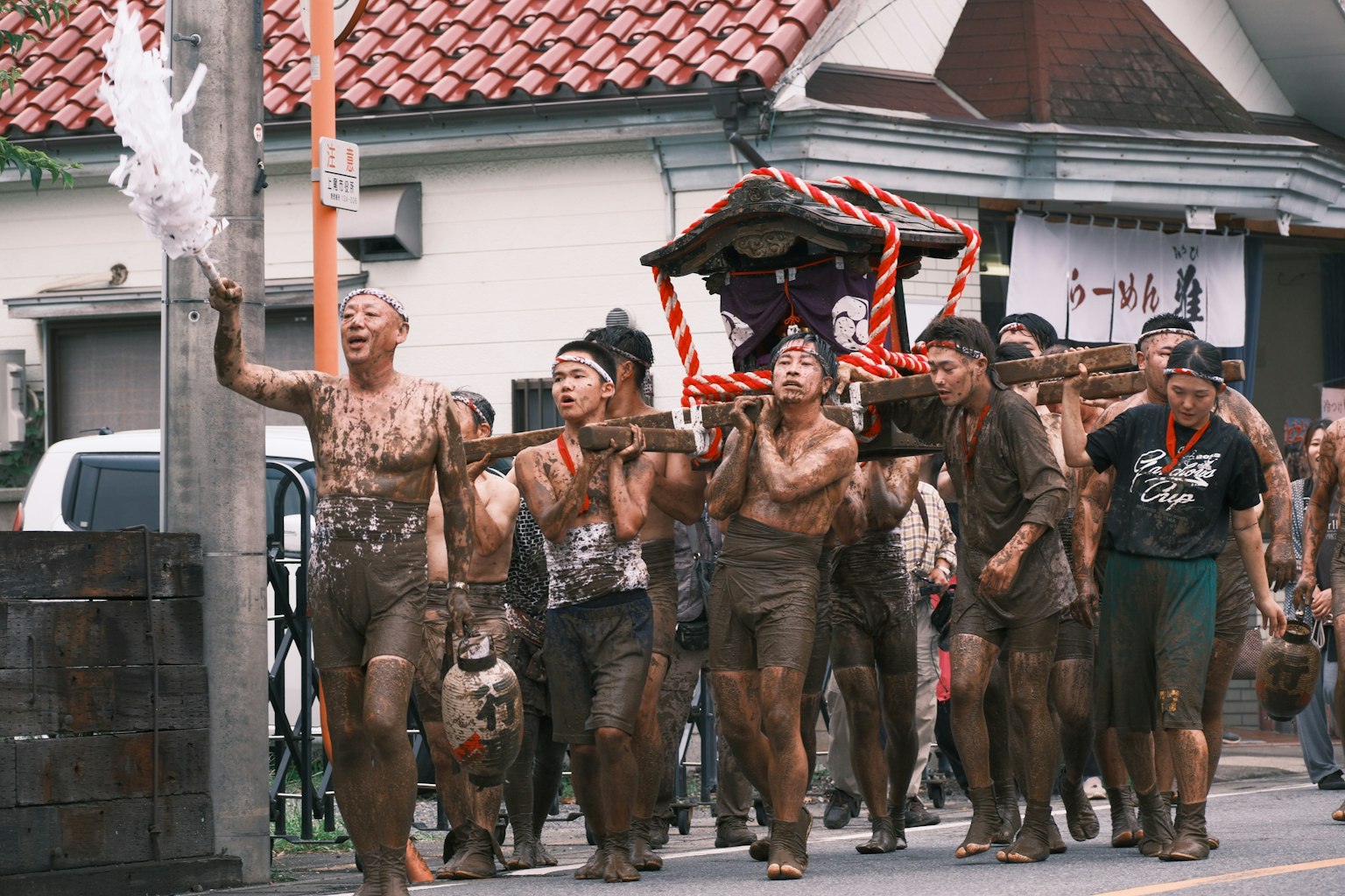 Uomini coperti di fango che portano un mikoshi durante un festival
