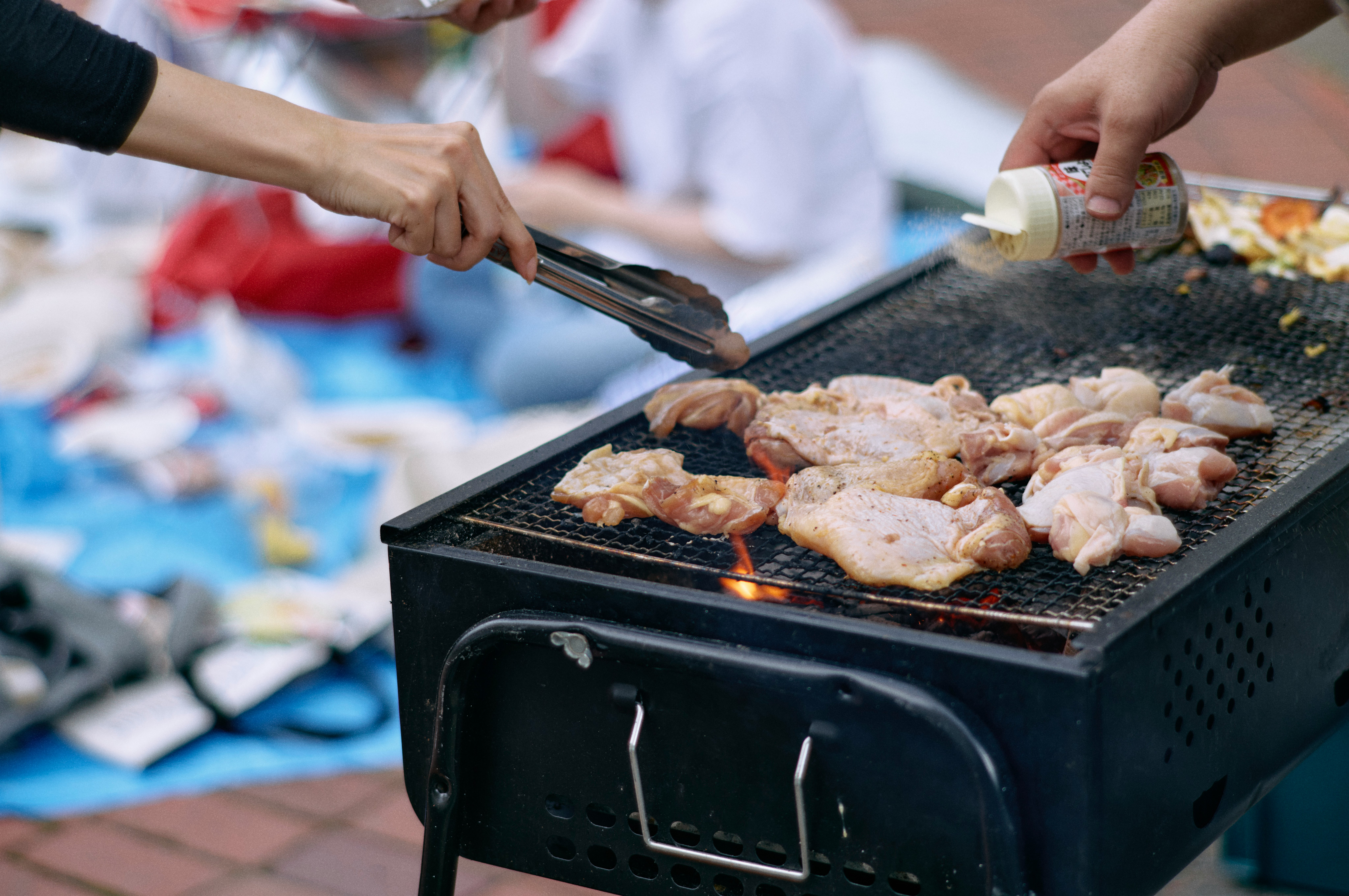 Hands grilling meat on an outdoor barbecue grill