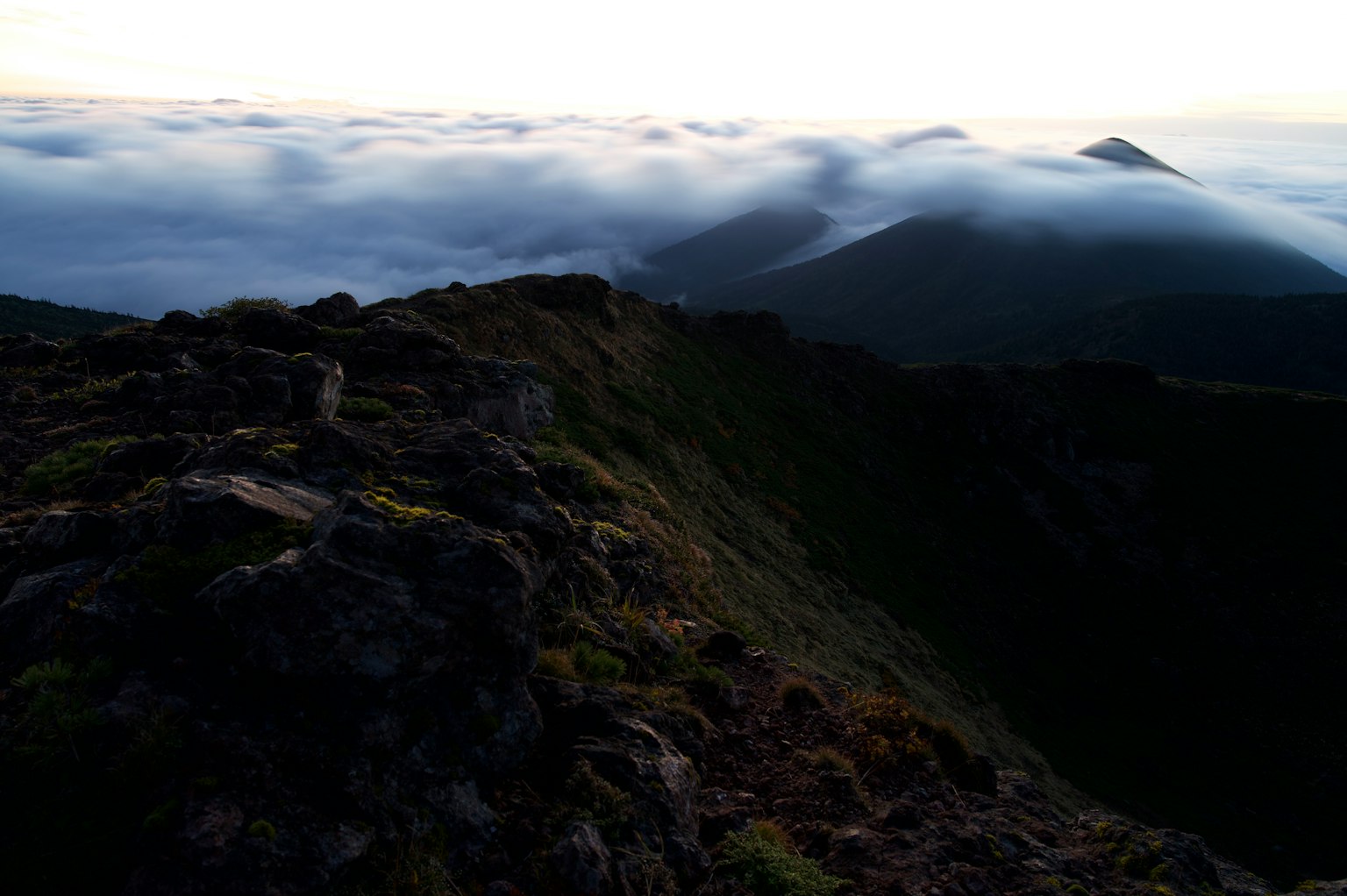 Cresta de montaña con un mar de nubes bajo la suave luz del amanecer