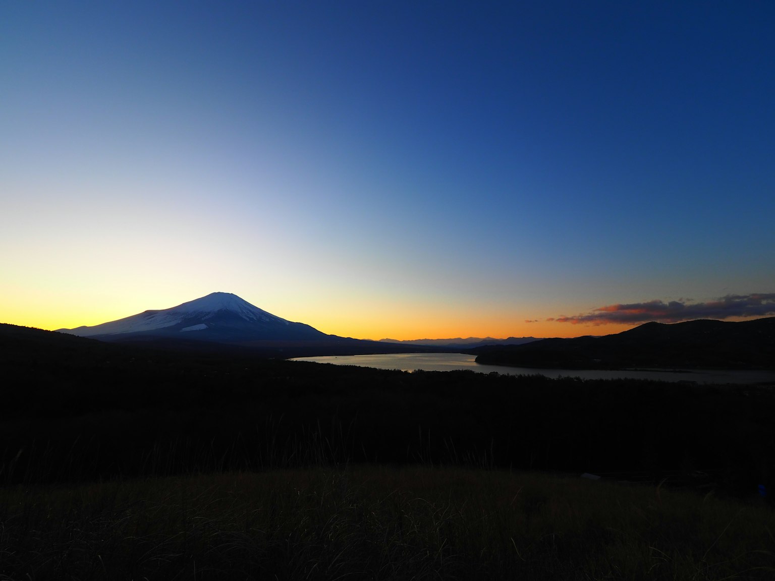 Vista panoramica di una montagna e un lago al tramonto con cielo sfumato