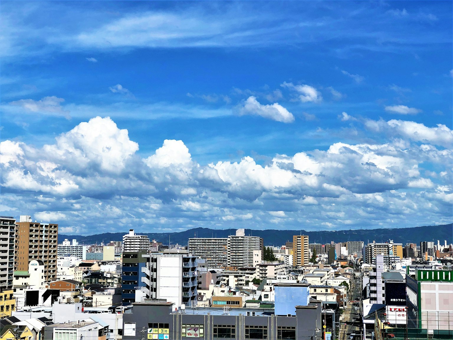 Cityscape with blue sky and fluffy white clouds featuring a mix of high-rise buildings and residential areas