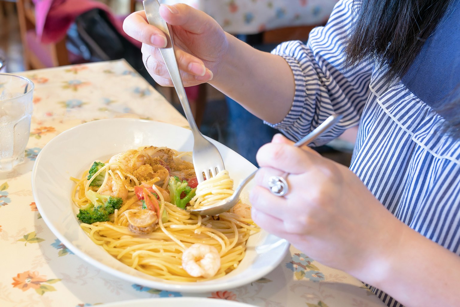 Kedekatan tangan yang menikmati spaghetti dengan seafood dan sayuran menggunakan garpu dan sendok