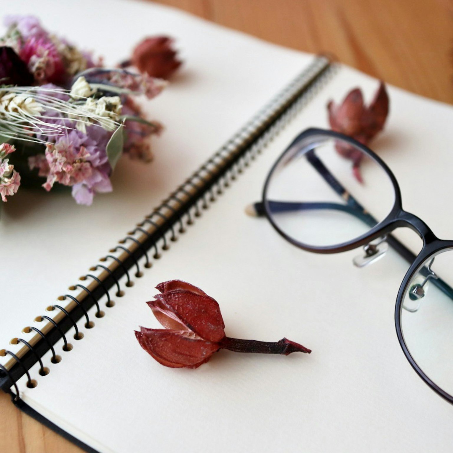 Brille und Trockenblumenarrangement auf einem Skizzenbuch