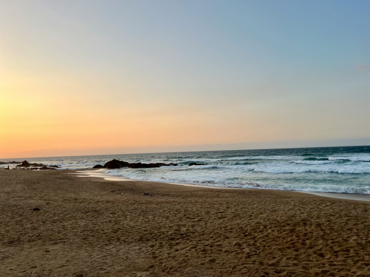 Schöne Strand-Sonnenuntergangsszene Wellen schlagen gegen den Sand sanfte Himmelstöne