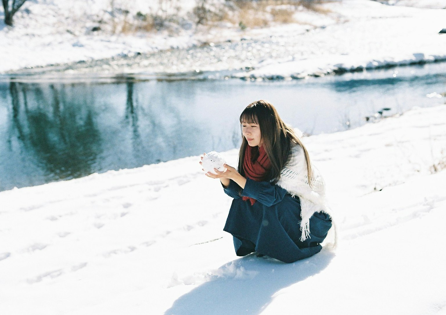 Femme accroupie dans la neige tenant de la neige dans ses mains