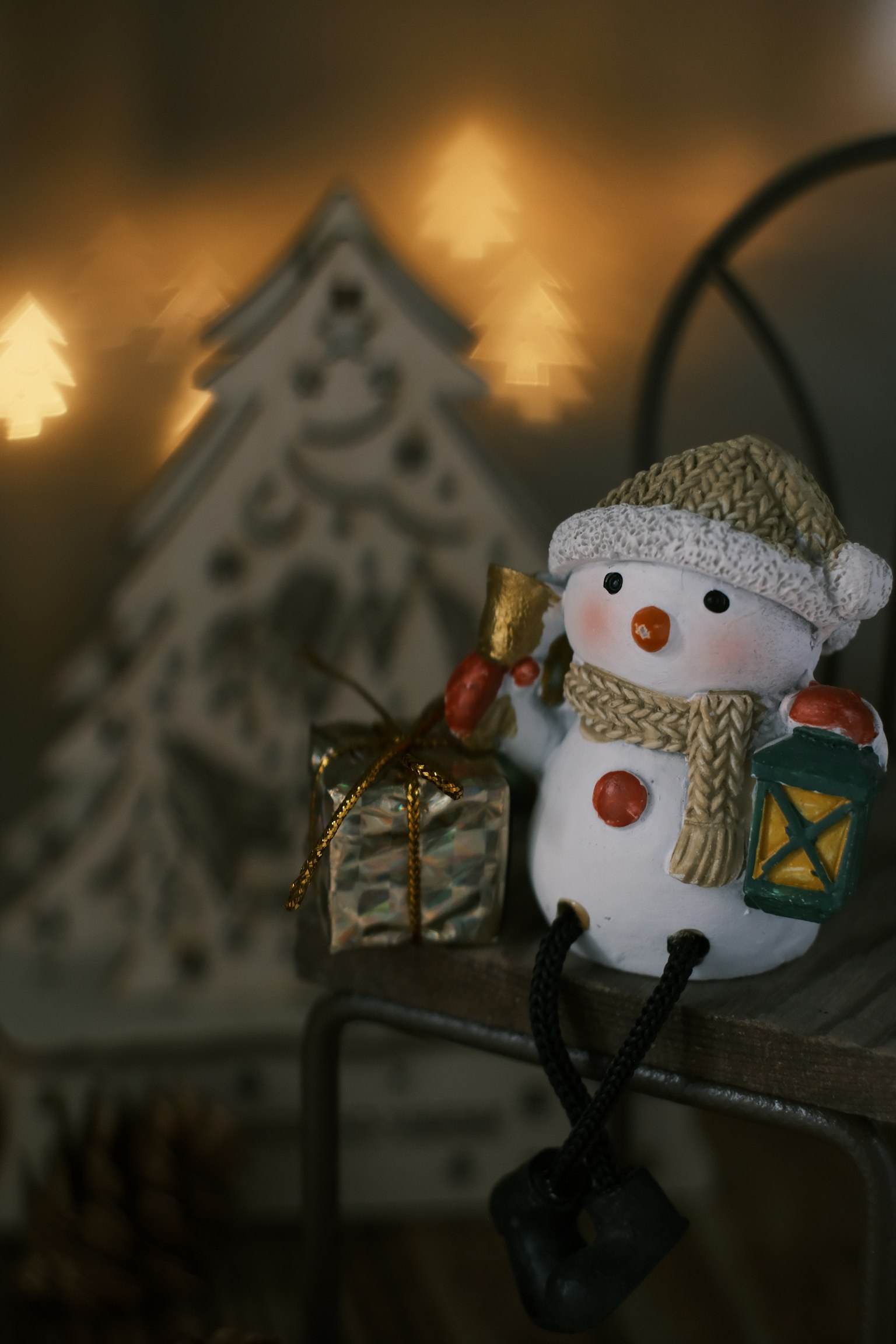 Un bonhomme de neige tenant un cadeau assis devant un arbre de Noël