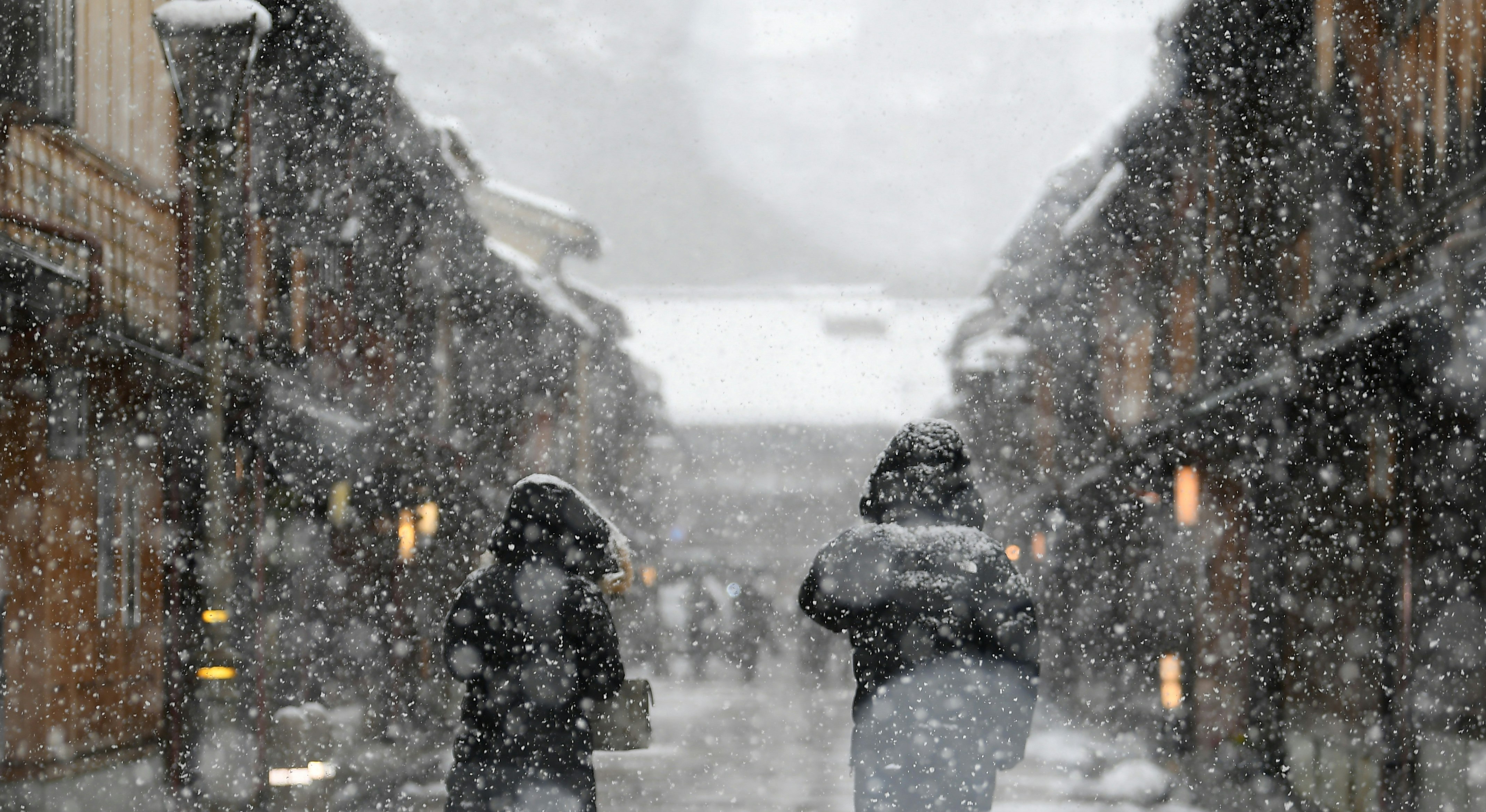 雪の降る街の路地を歩く人々