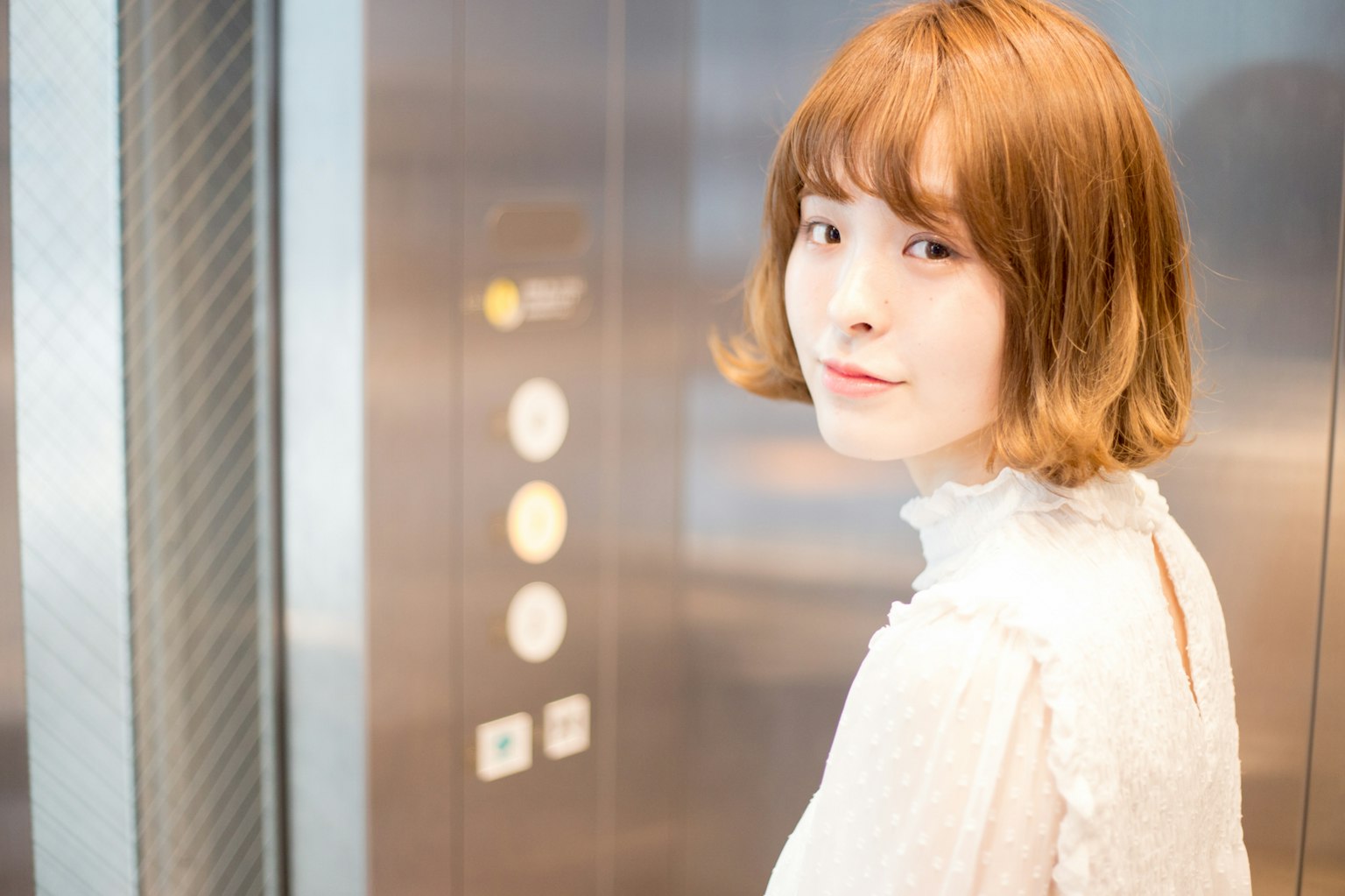 엘리베이터에서 돌아보고 있는 여성의 초상 밝은 머리와 흰색 의상