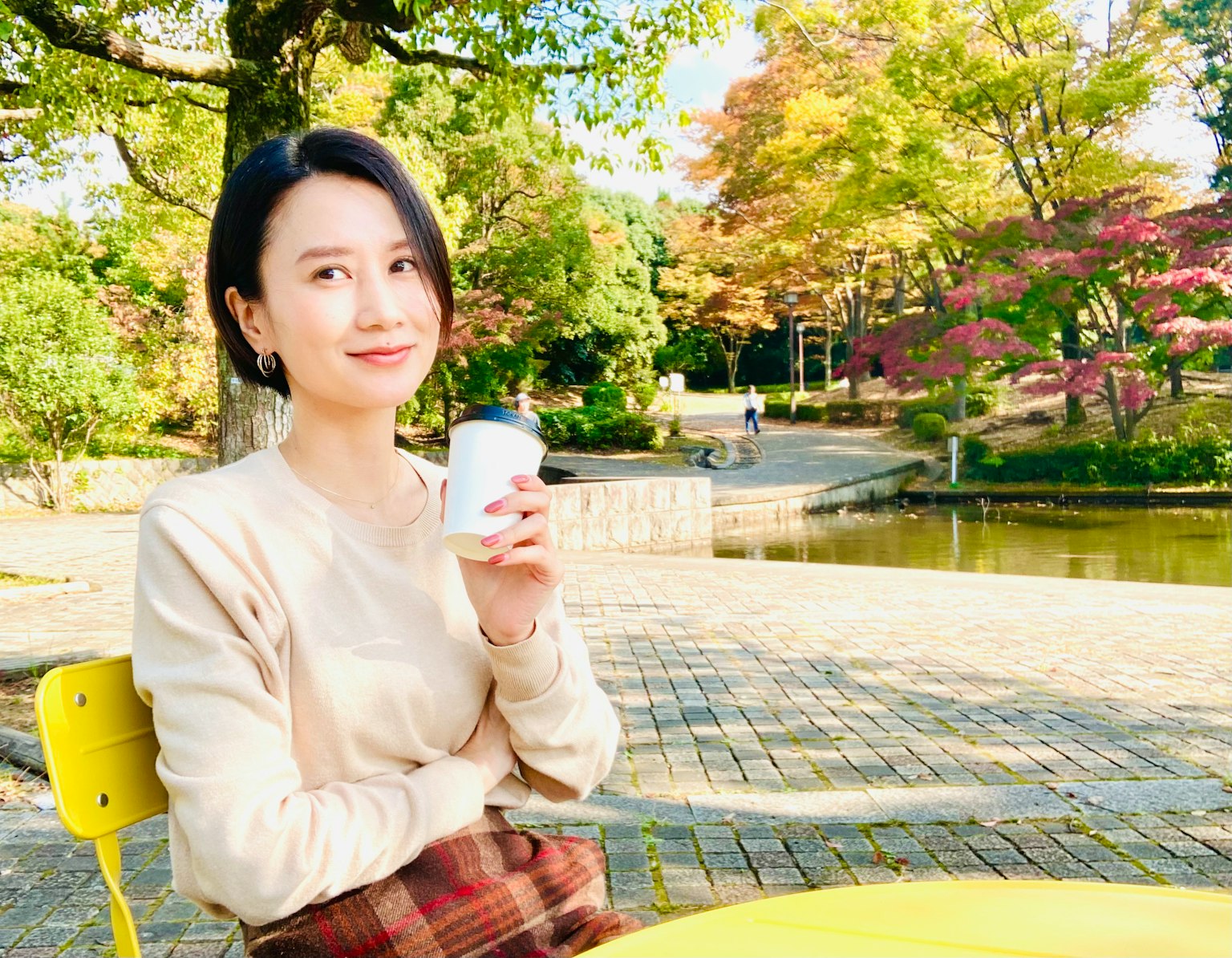 一位女性坐在公園長椅上，手持咖啡杯微笑