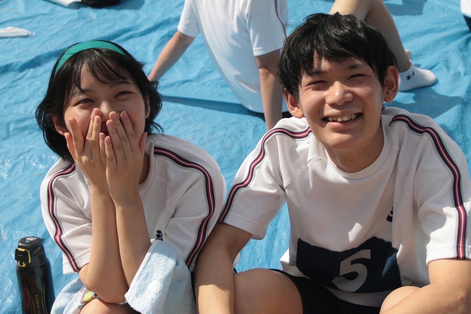 Ragazzo e ragazza sorridenti seduti su un tappeto blu durante un evento sportivo
