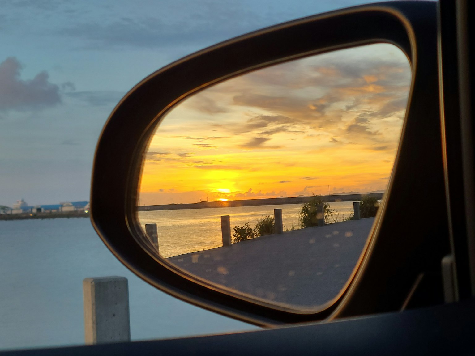 Tramonto riflesso nello specchietto laterale di un'auto su una superficie d'acqua calma