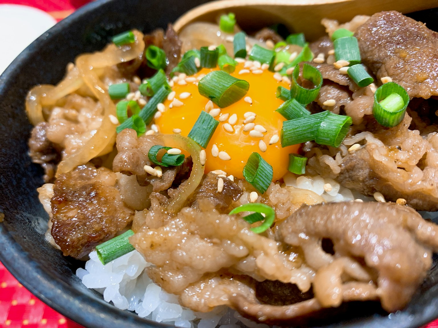 Một bát cơm topped với thịt bò và lòng đỏ trứng sống trang trí bằng hành lá và hạt mè
